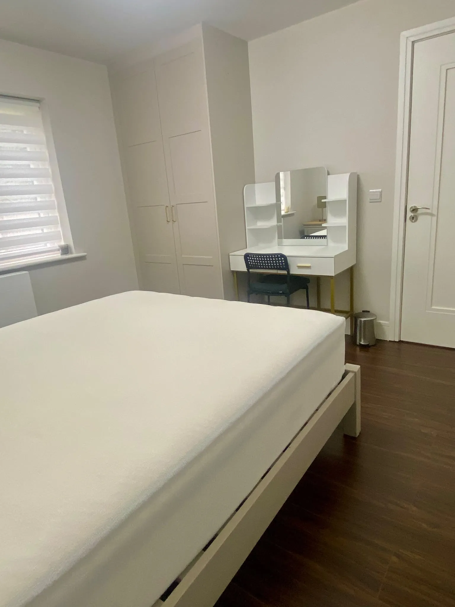 Bedroom with a bed in the foreground, built-in wardrobe on the left, and a dressing table with mirror and chair against the wall.