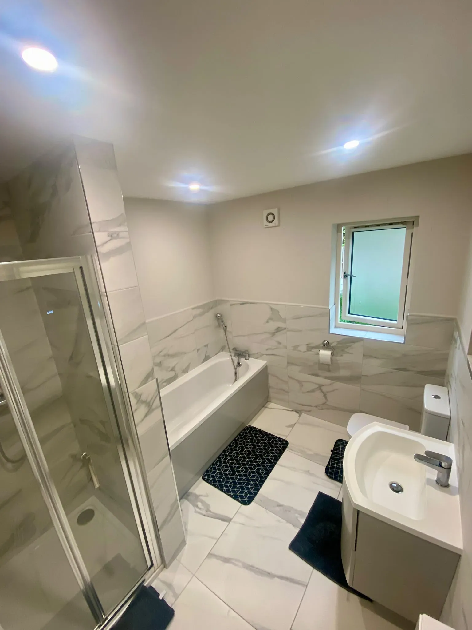 Bathroom with a bathtub, separate glass shower enclosure, sink, toilet, and a small frosted window.