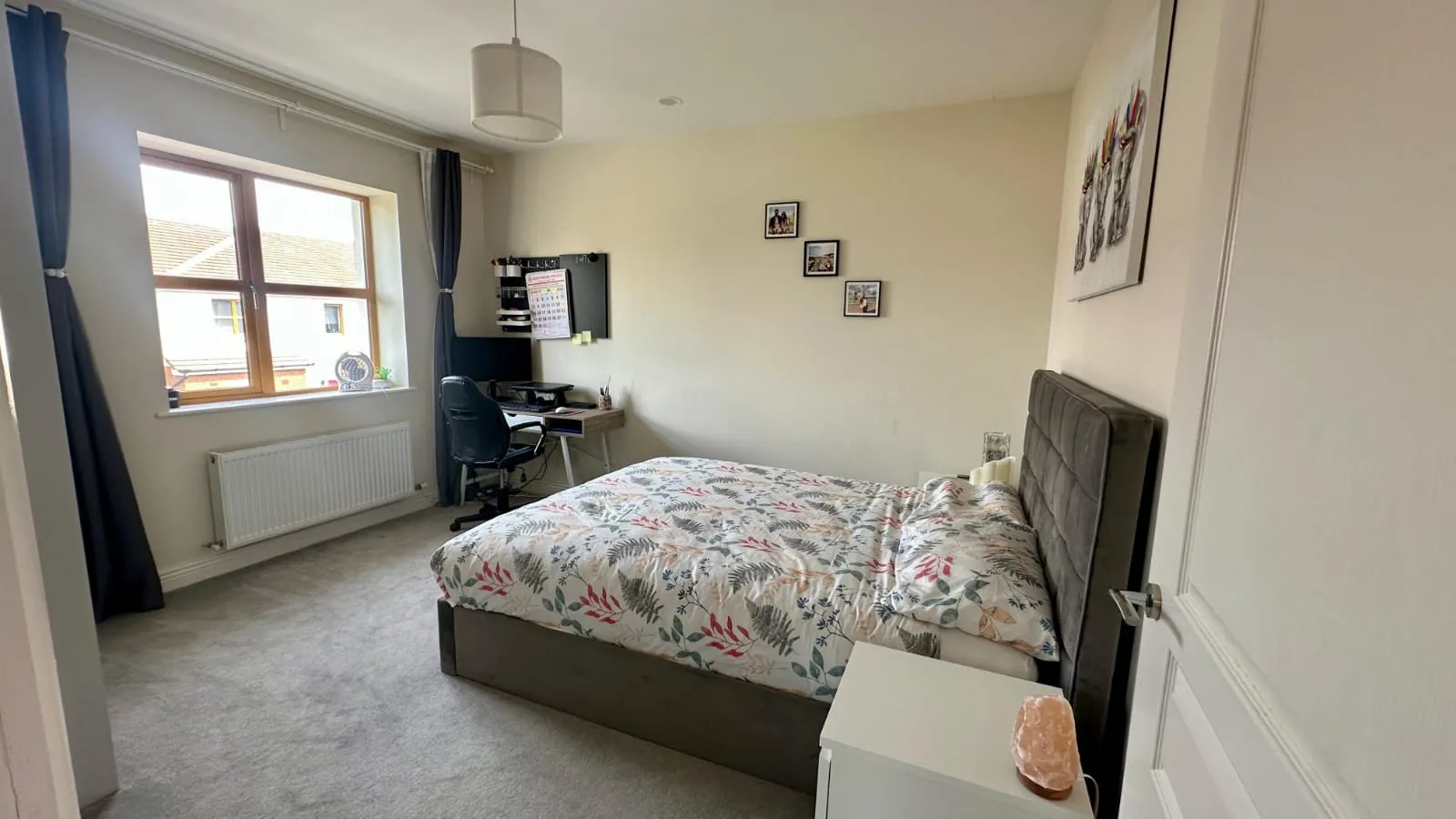 Bedroom with a double bed, bedside table, desk and office chair by a window with curtains