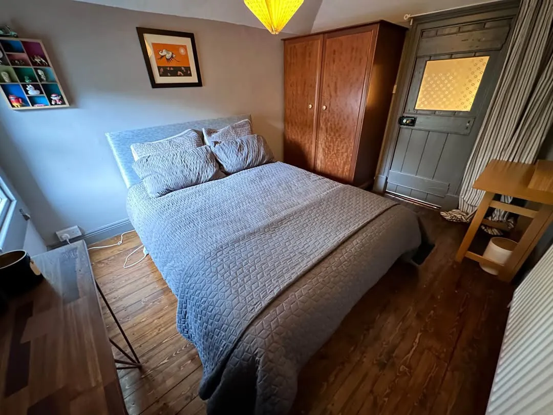 Bedroom with a double bed covered in a quilt, two pillows, wooden wardrobe, bedside table and a door with patterned glass.