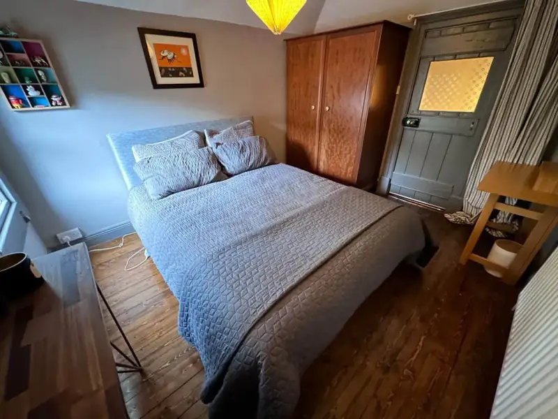 Bedroom with a double bed covered in a quilt, two pillows, wooden wardrobe, bedside table and a door with patterned glass.
