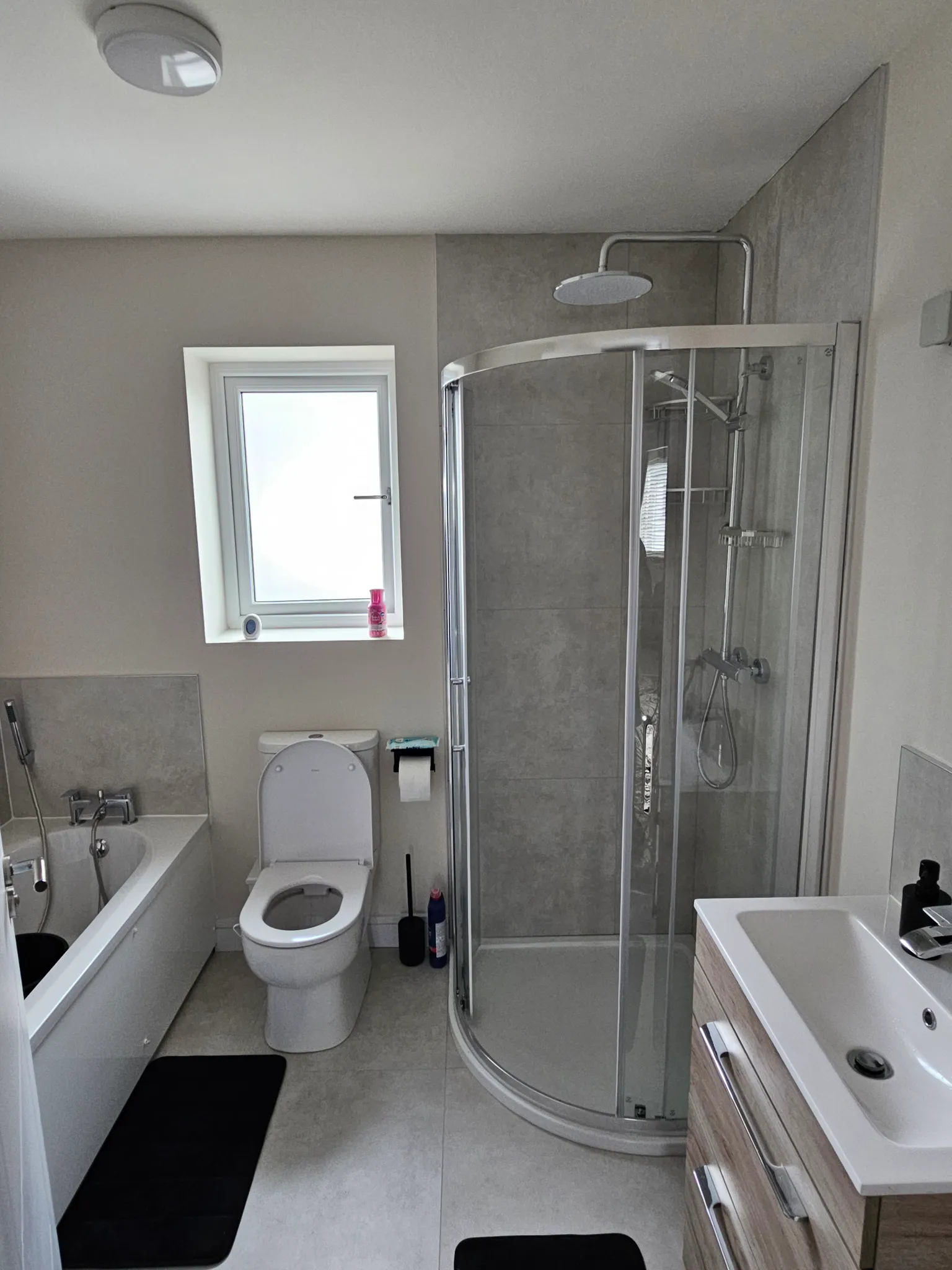 Bathroom with a corner glass shower enclosure, toilet, bathtub, sink cabinet, and a small window above the toilet.