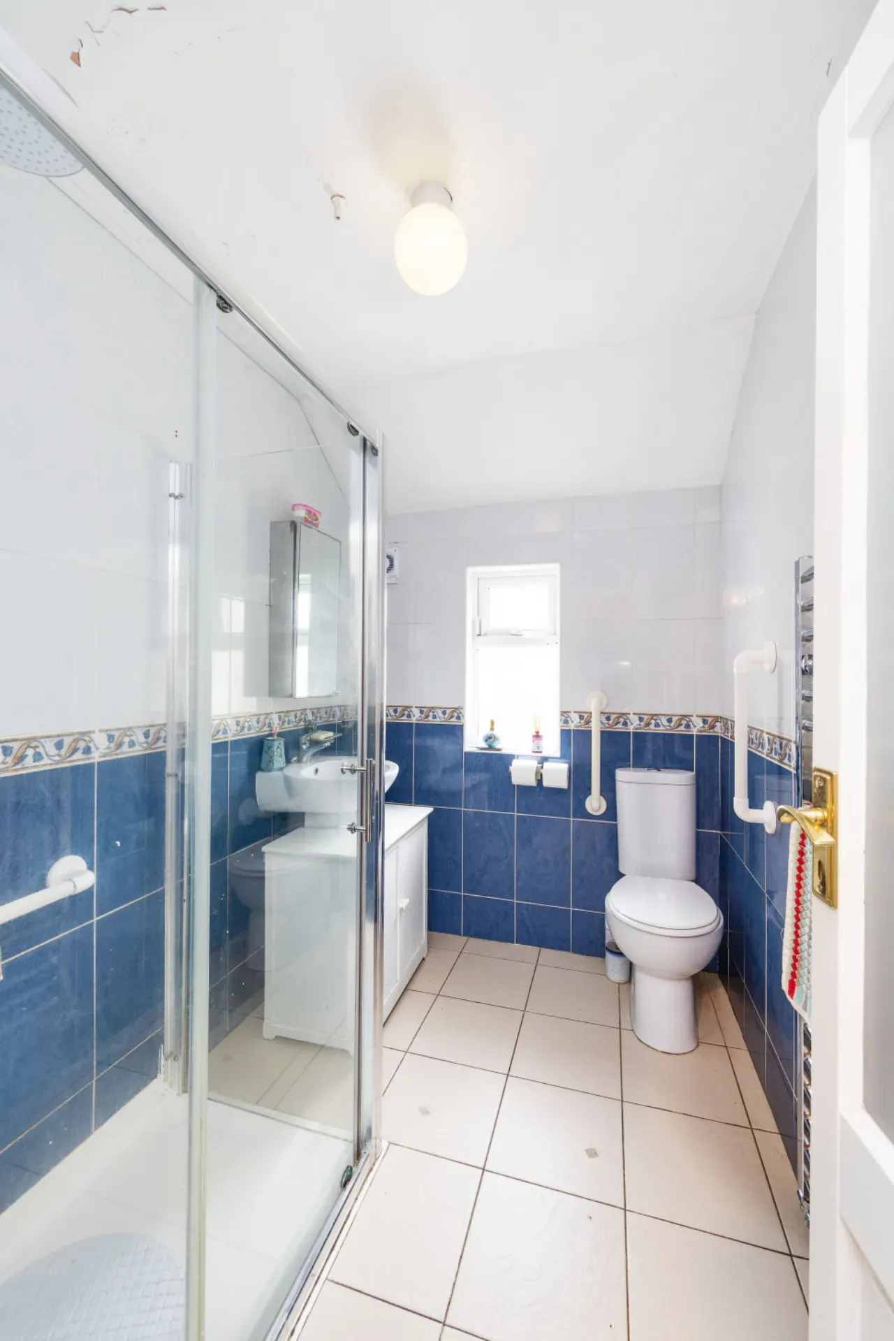 Bathroom with a corner shower enclosure, sink with mirrored cabinet, toilet, small window, and blue tiled lower walls