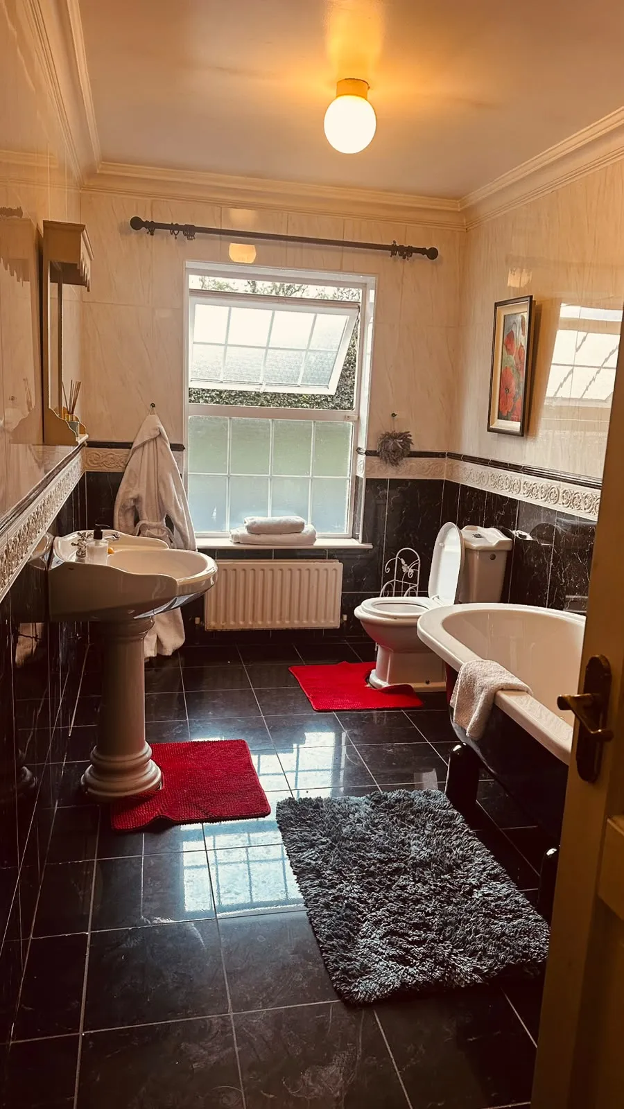 Bathroom with a freestanding bathtub, pedestal sink, toilet, window, and several floor rugs.