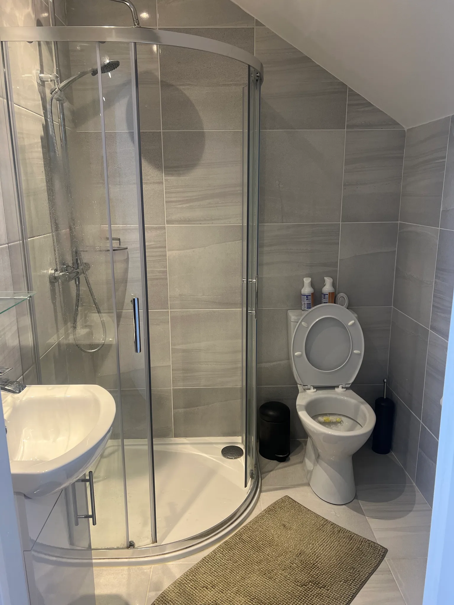 Bathroom with a corner glass shower, toilet with open seat, and sink
