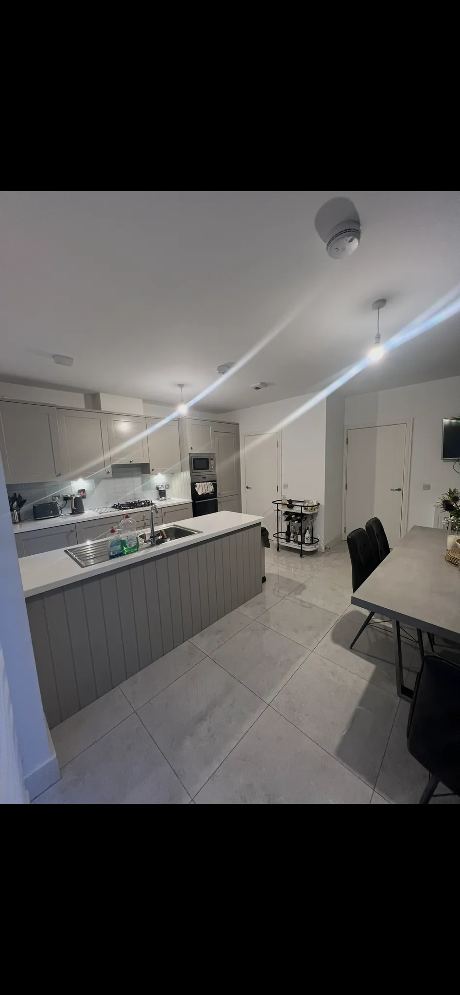 Kitchen with a central island and sink, built-in oven and cabinets along the back wall, and a dining table with chairs to the right.