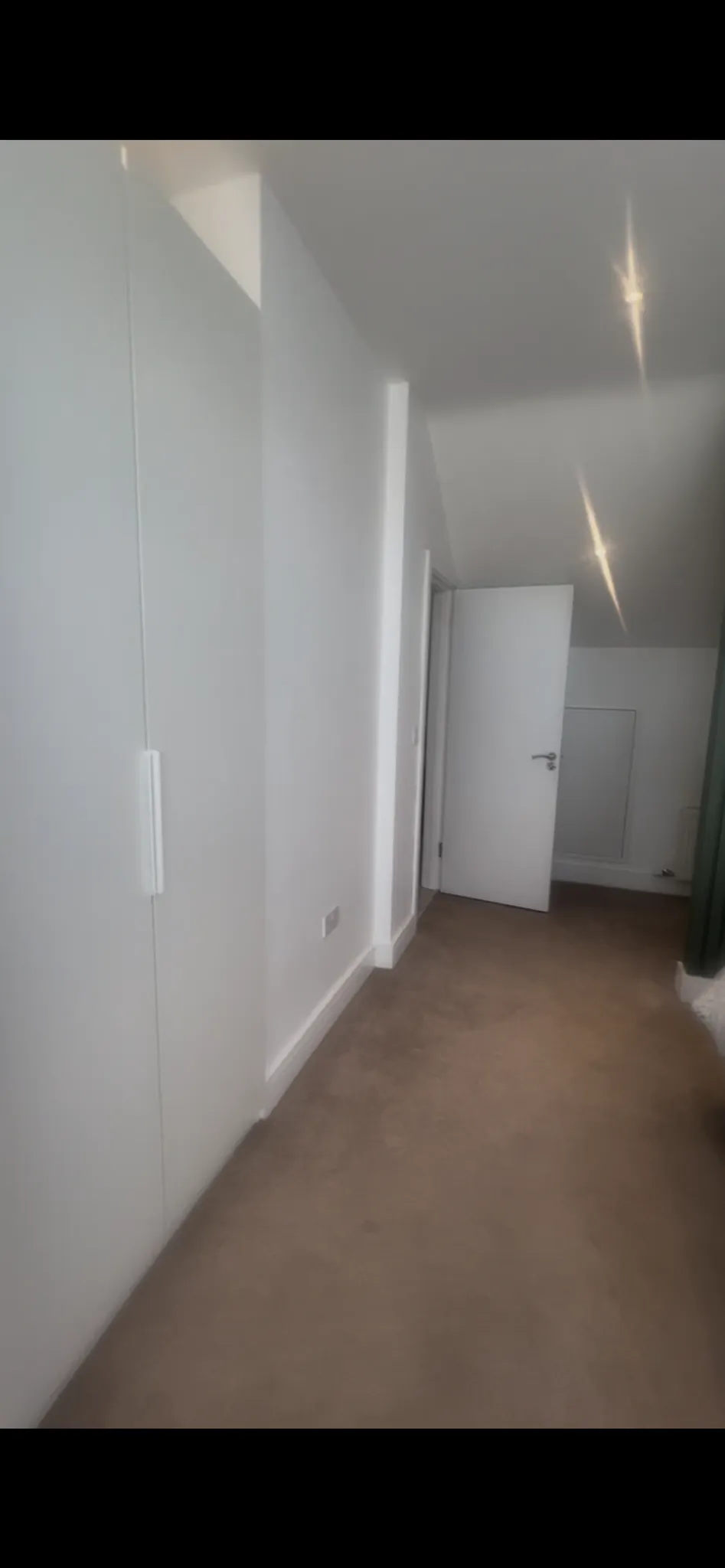 Narrow hallway with carpeted floor, white walls, built-in wardrobe on the left and an open white door at the end.