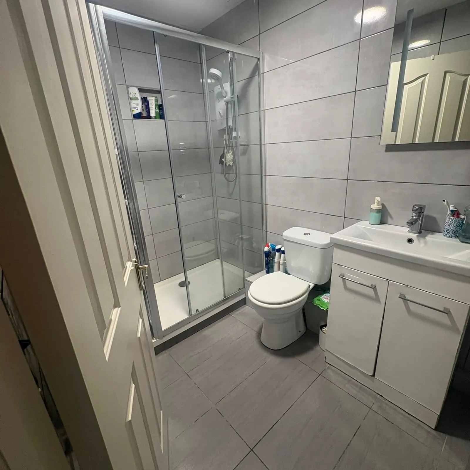 Bathroom with a glass-enclosed shower, toilet, sink with vanity and mirror, and tiled walls and floor.