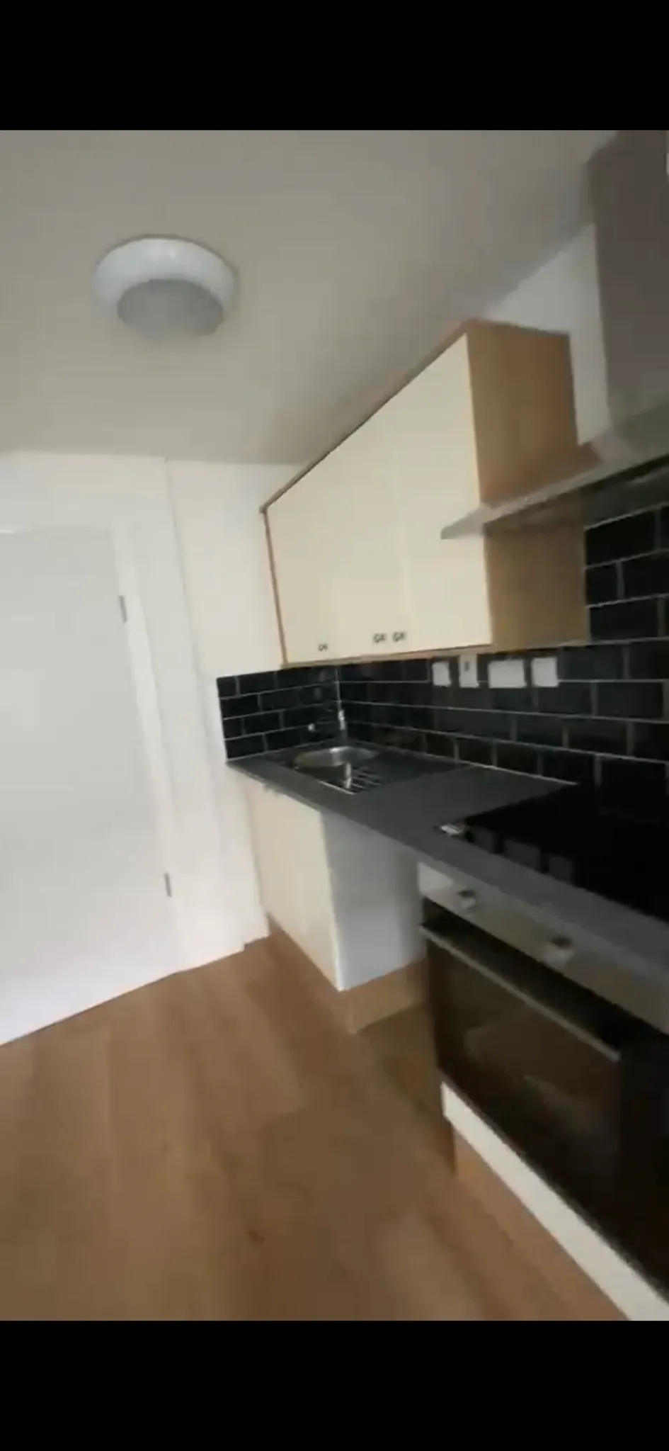 Kitchen with countertop, sink, oven, upper cabinets and black tiled backsplash