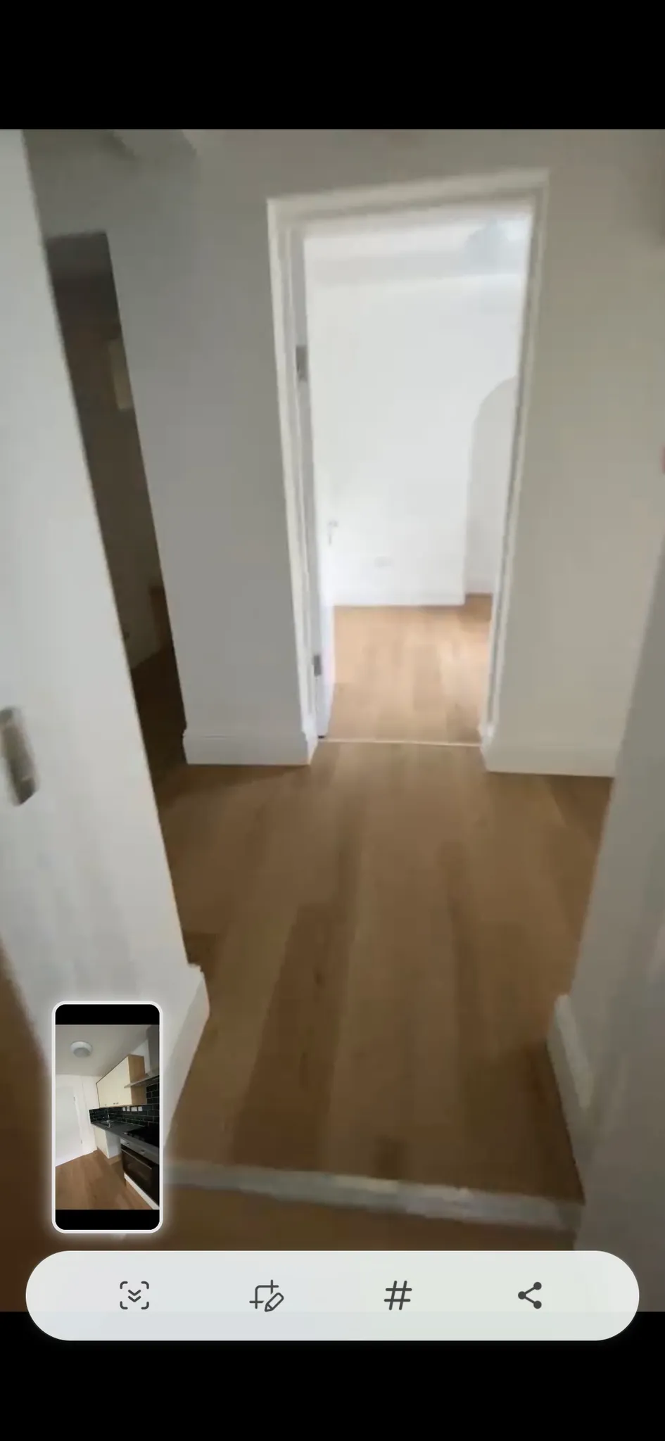 Hallway with wood flooring leading to an open doorway into another empty room with white walls