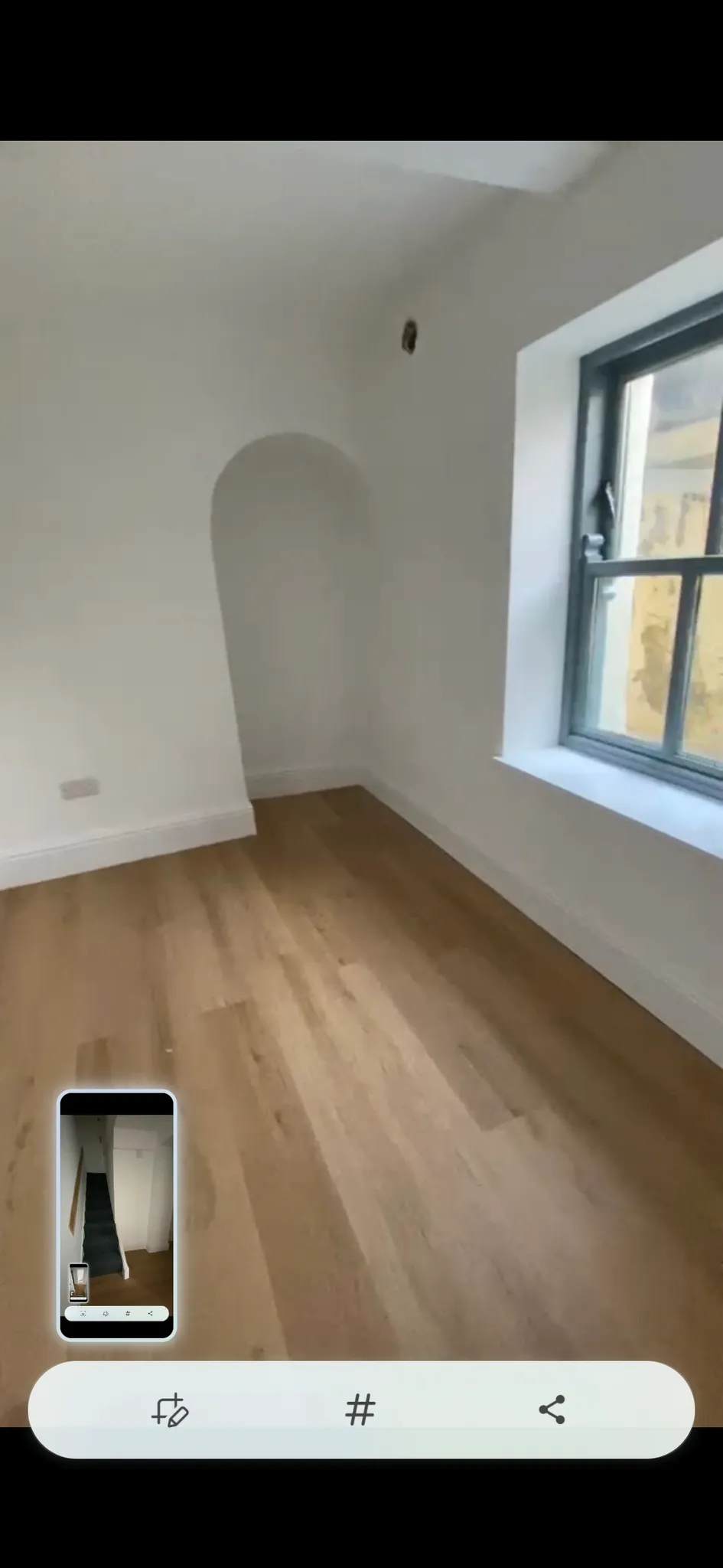 Empty room with a wooden floor, white walls, a recessed arched alcove and a window at right