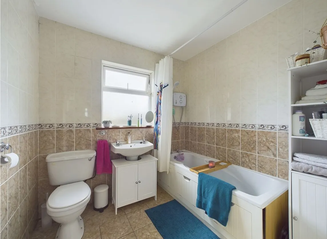 Bathroom with a bathtub and shower, sink with cabinet, toilet, window, and shelving with towels and toiletries