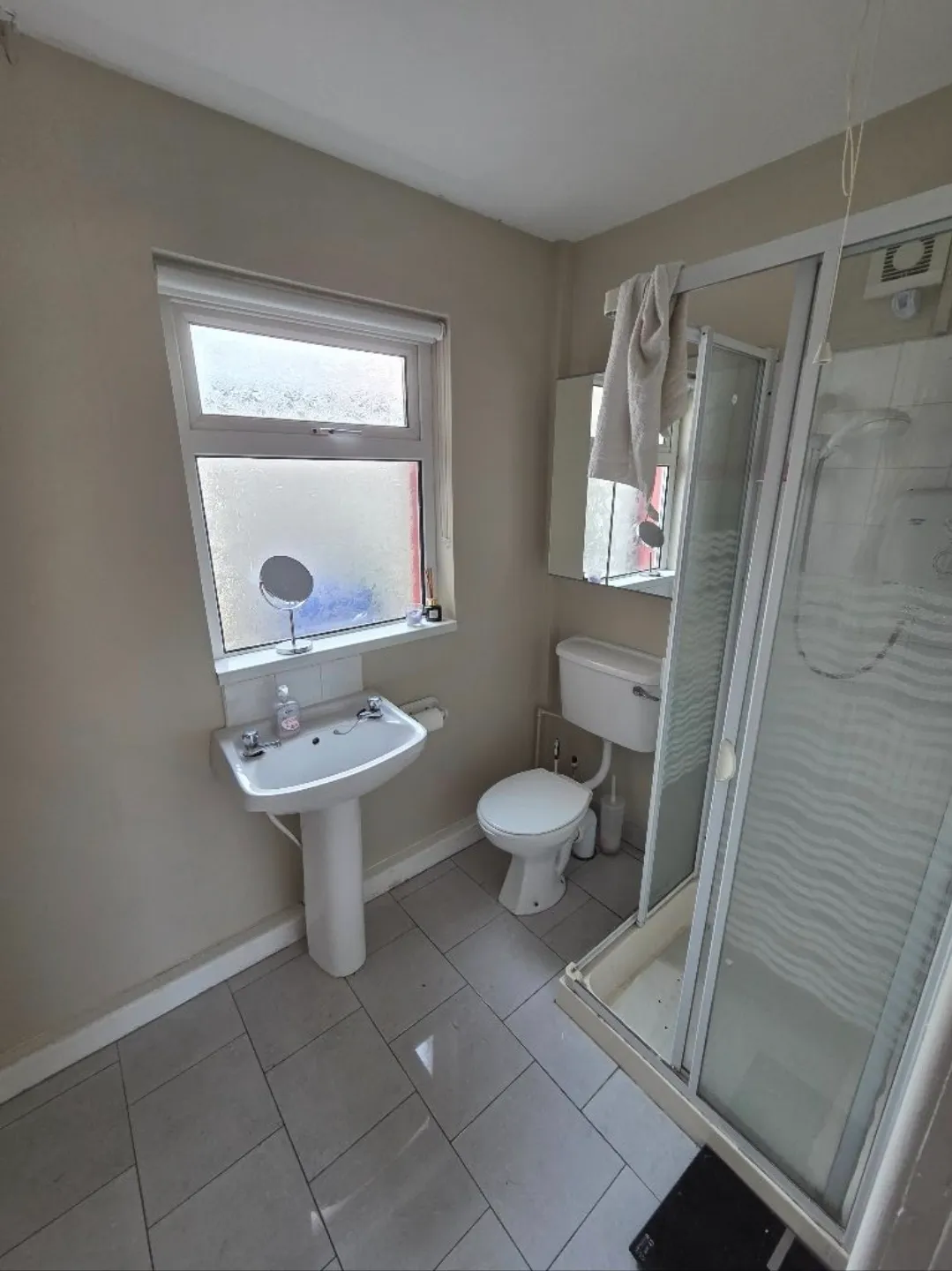 Bathroom with a pedestal sink, toilet, frosted window, mirrored cabinet, and corner shower with sliding door.