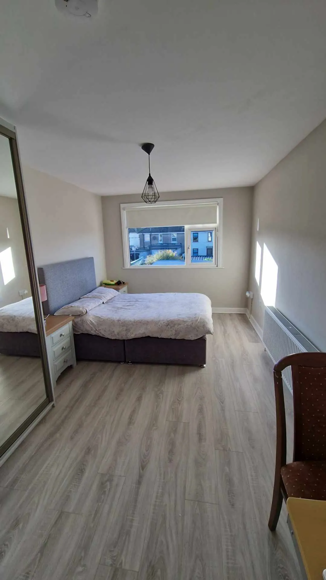 Bedroom with a double bed, bedside table, mirrored wardrobe, window, radiator and pendant ceiling light.