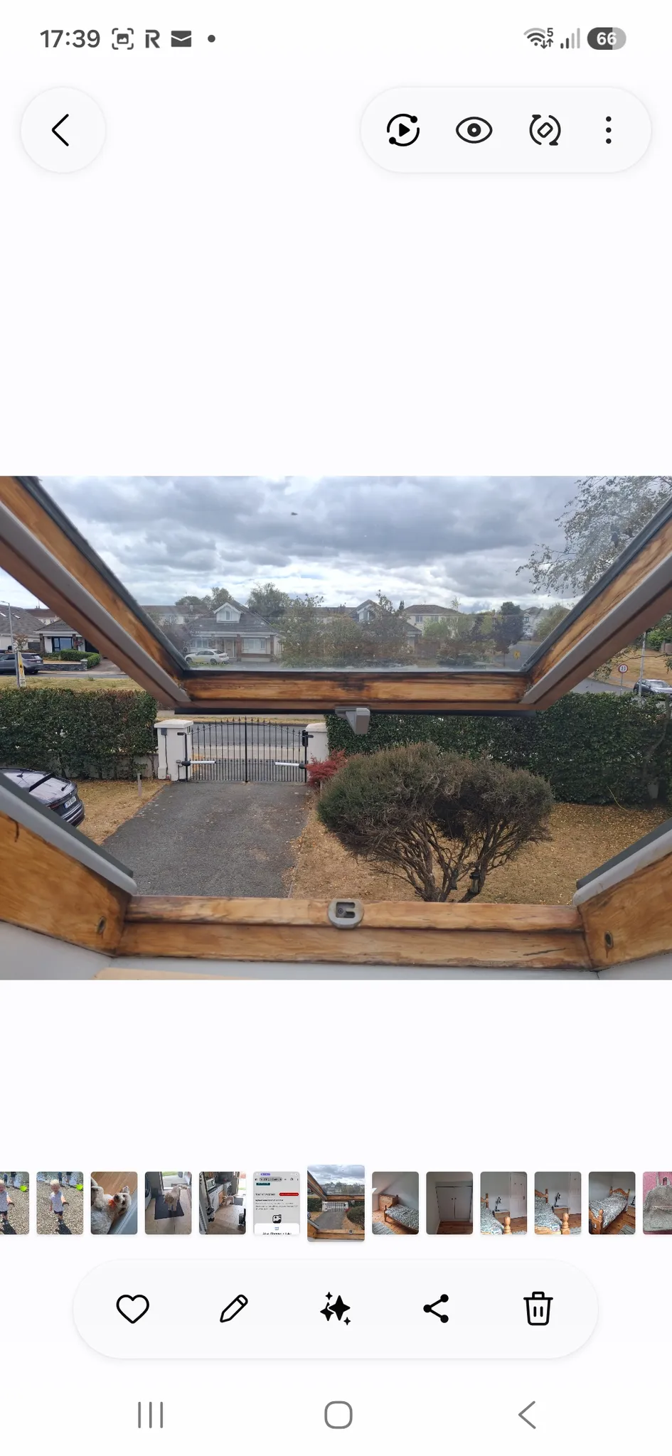 View through an open roof window/skylight onto a driveway, gate, hedge and neighboring houses under an overcast sky.
