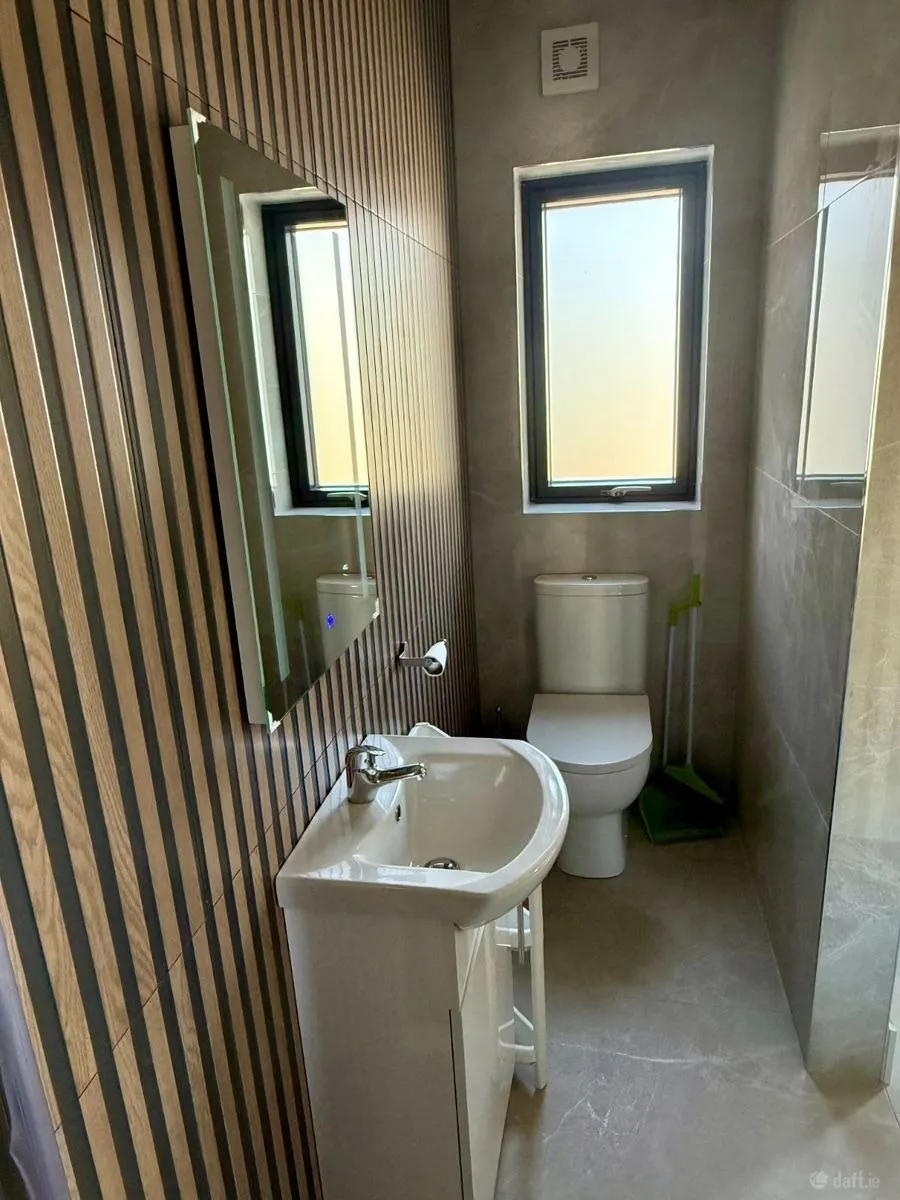 Small bathroom with a wall-mounted mirror, sink with cabinet, toilet, narrow frosted window, and vertical wood-panel wall