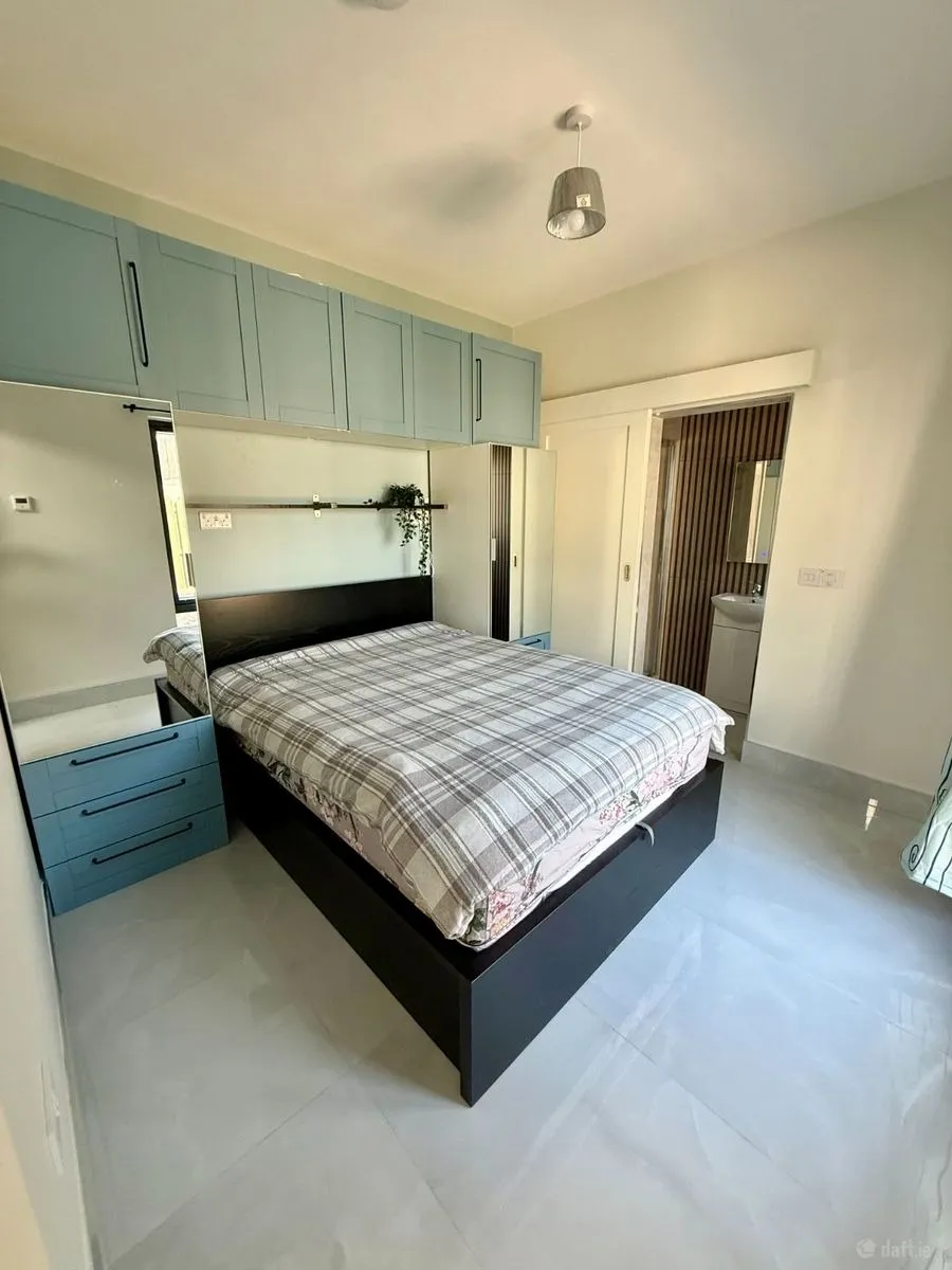 Bedroom with a double bed, overhead blue cabinets, mirrored wardrobe doors, bedside drawers, and a doorway to a bathroom.