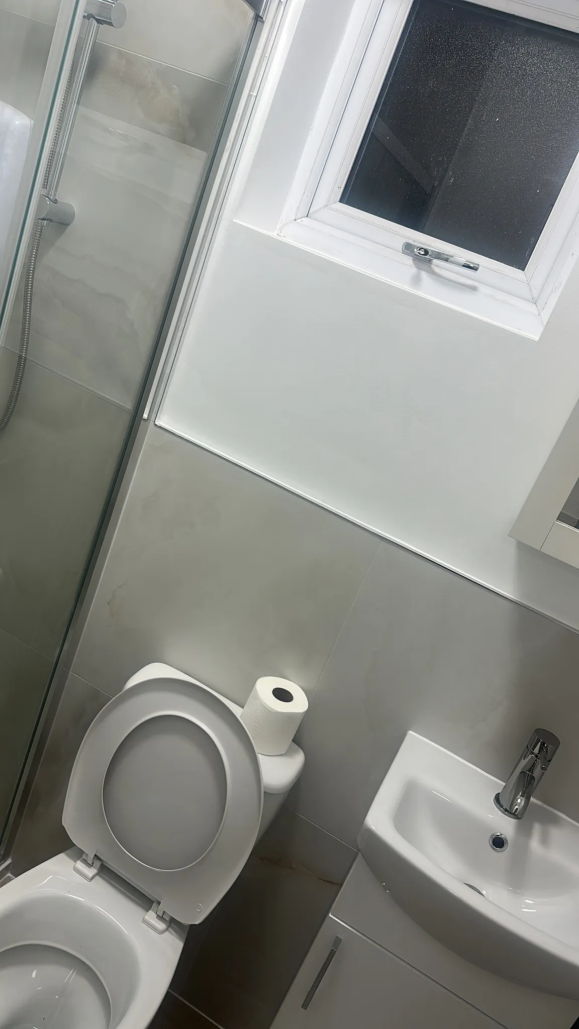 Bathroom with toilet, pedestal sink, shower enclosure with glass door, and window with dark blind