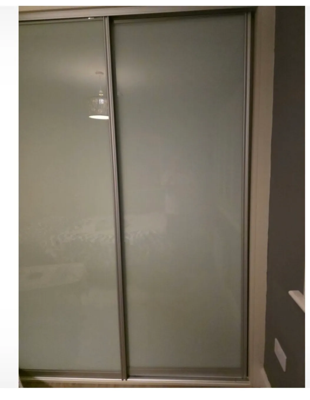 Sliding frosted glass closet doors with a metal frame and a faint lamp reflection