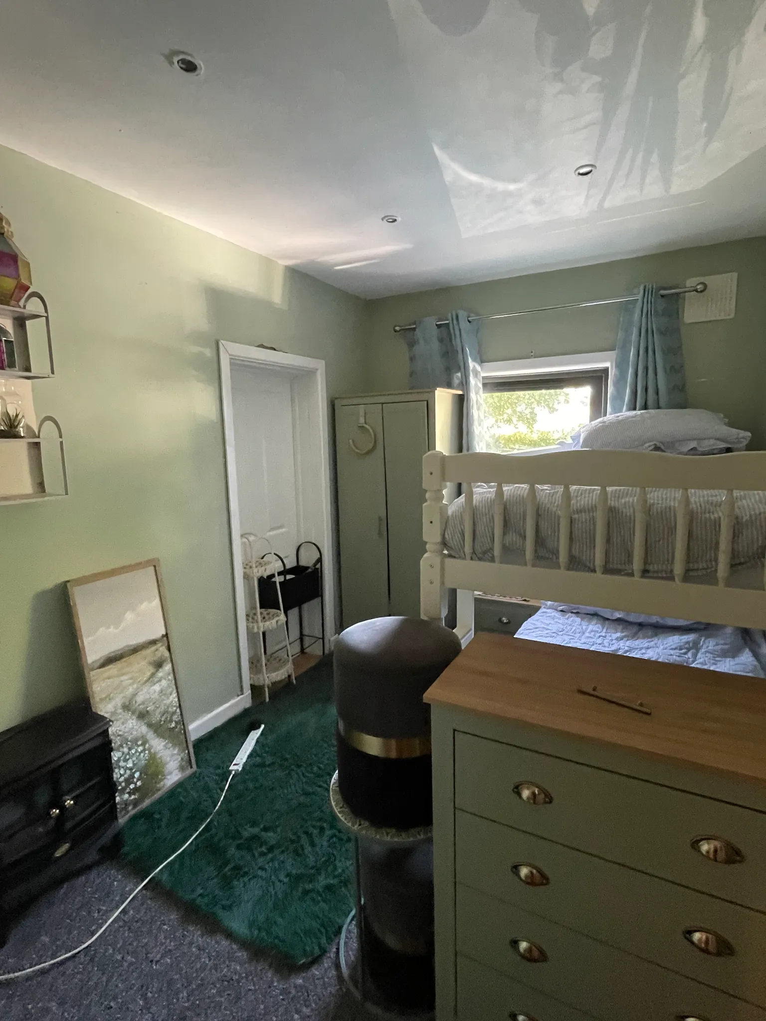 Bedroom with a bunk bed near a window with curtains, green painted walls, a dresser and a wardrobe.