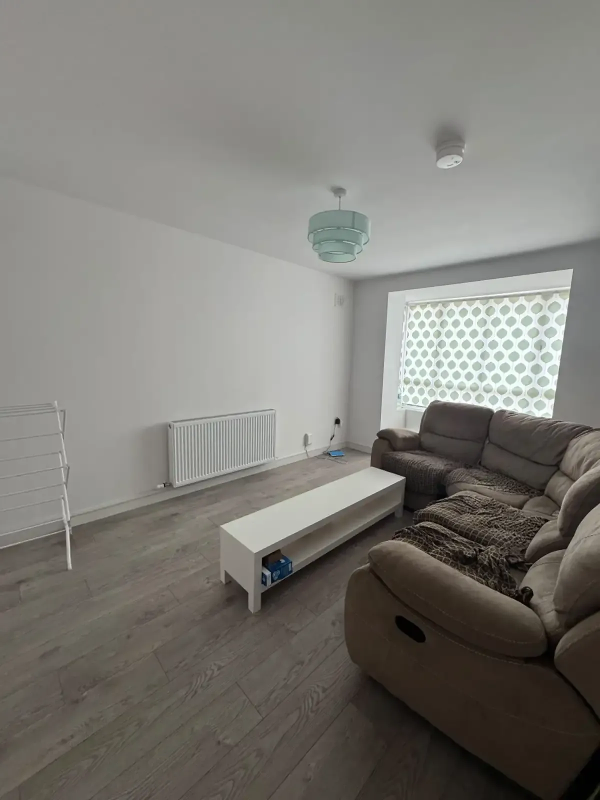 Living room with an L-shaped sofa, white low coffee table and a window with a patterned blind.
