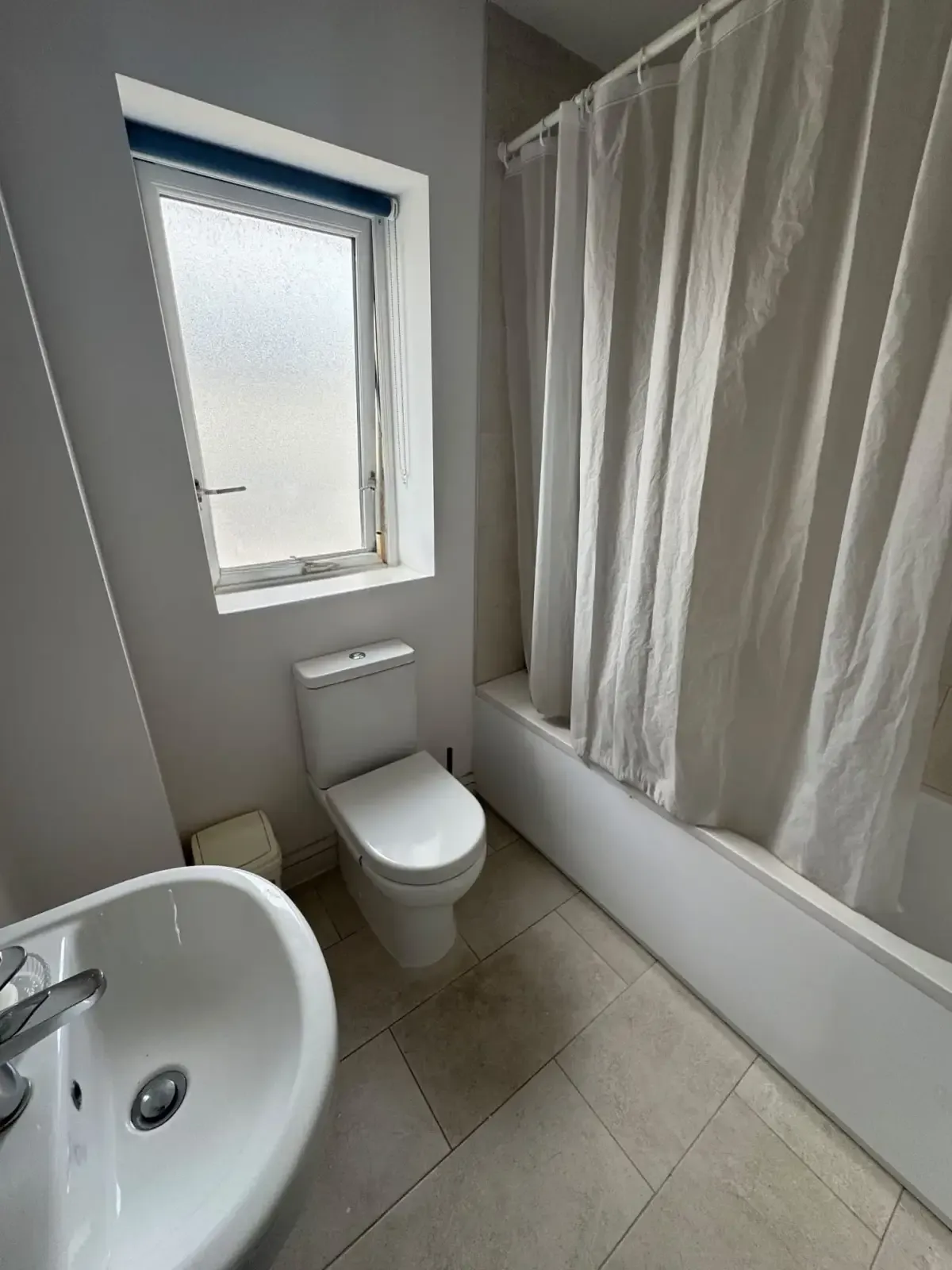 Bathroom with a toilet, sink in foreground, bathtub with a closed shower curtain, and a frosted window.