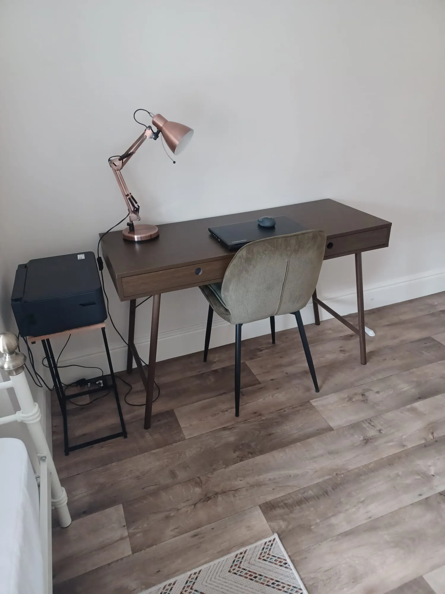 Workspace with a wooden desk, upholstered chair, adjustable desk lamp, closed laptop and a printer on a small stand