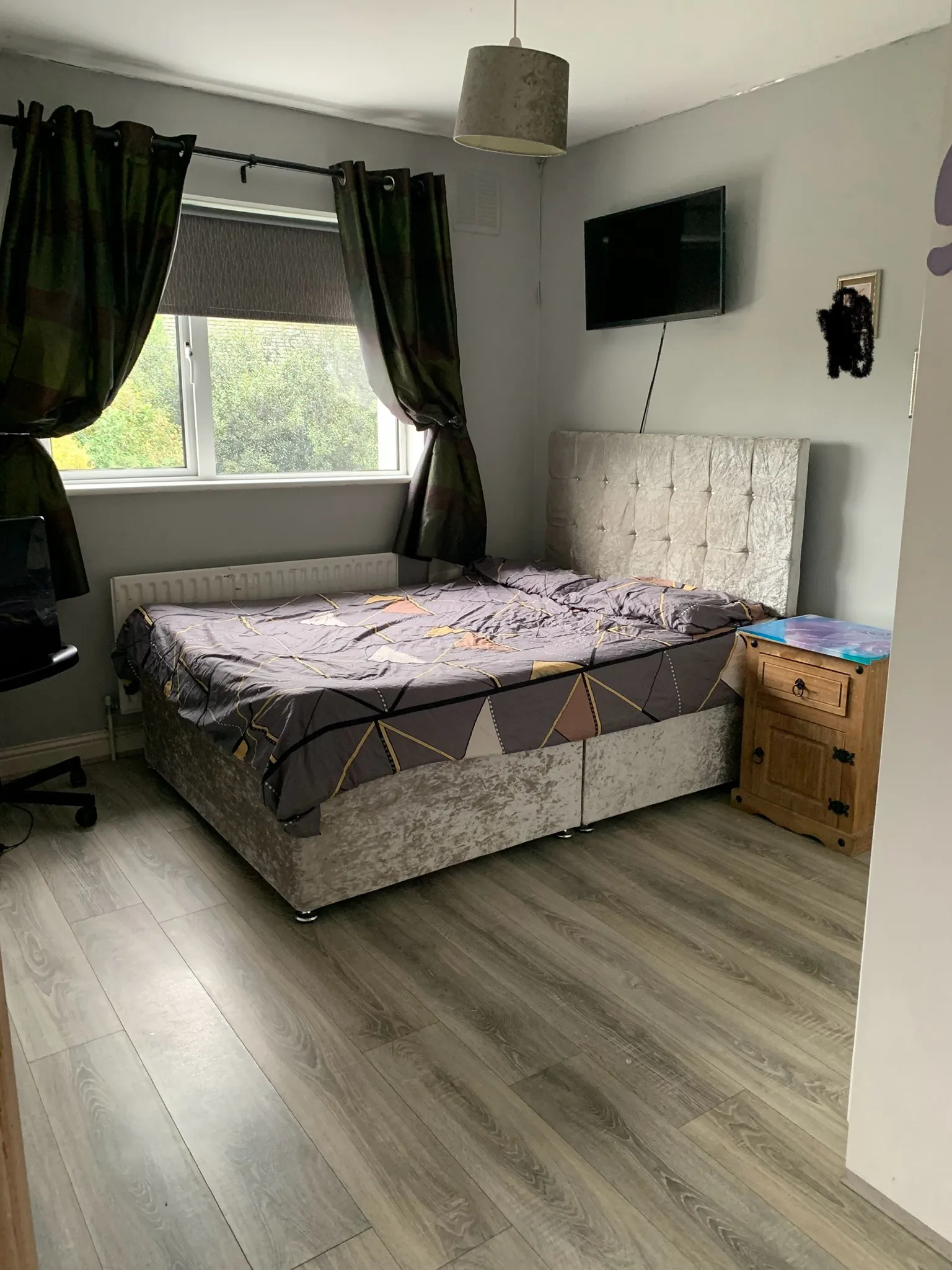 Bedroom with a double bed, upholstered headboard, window with curtains and a wall-mounted TV