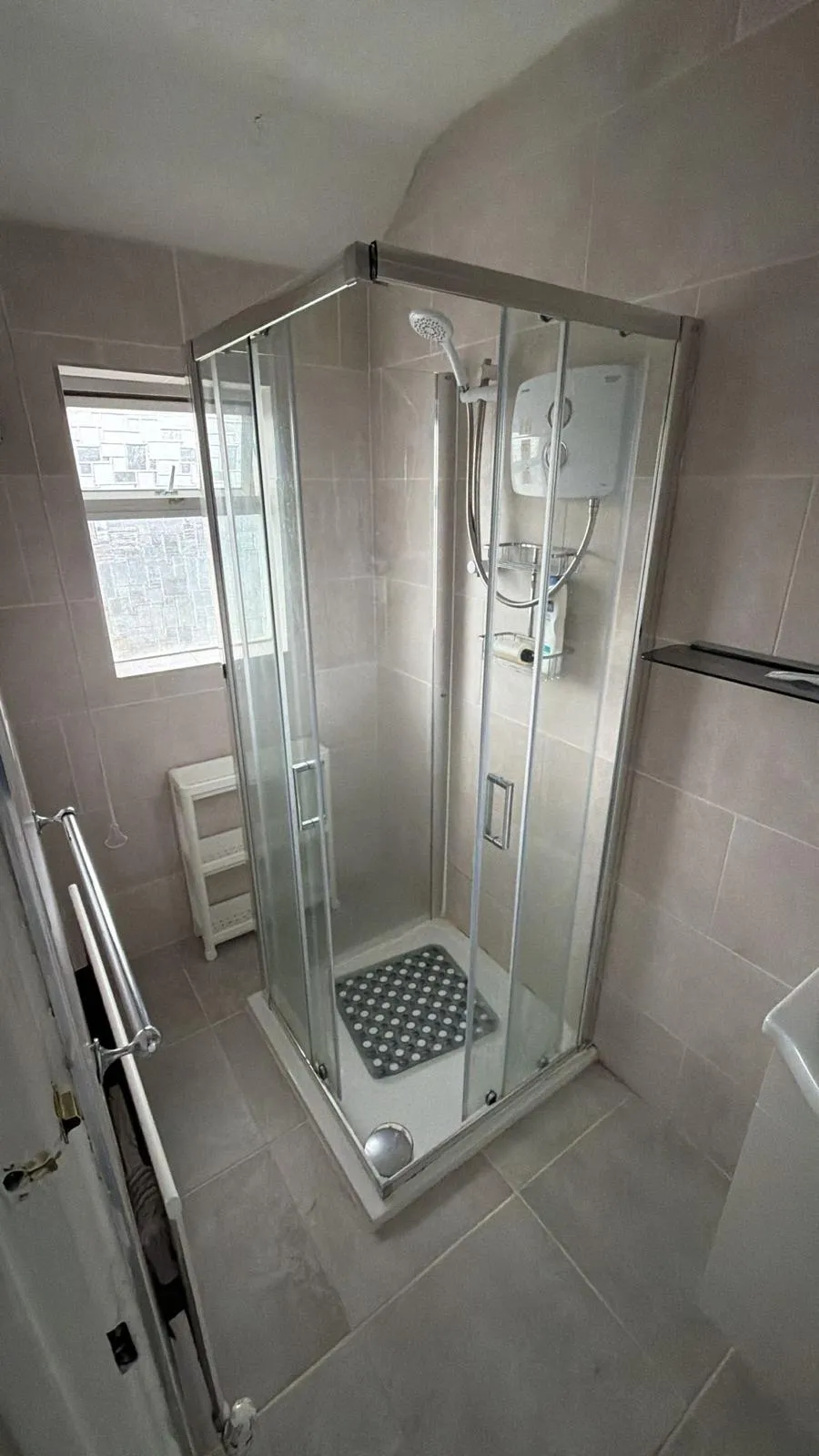 Bathroom with a corner glass-enclosed shower, wall-mounted electric shower unit, tiled walls and a small frosted window