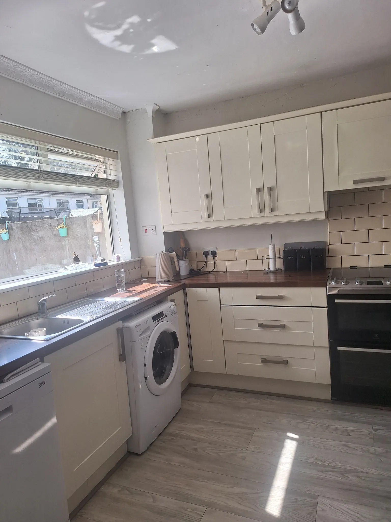 Kitchen with white cabinets, wooden countertop, stainless sink under a window with blinds, front-loading washing machine and a black oven.