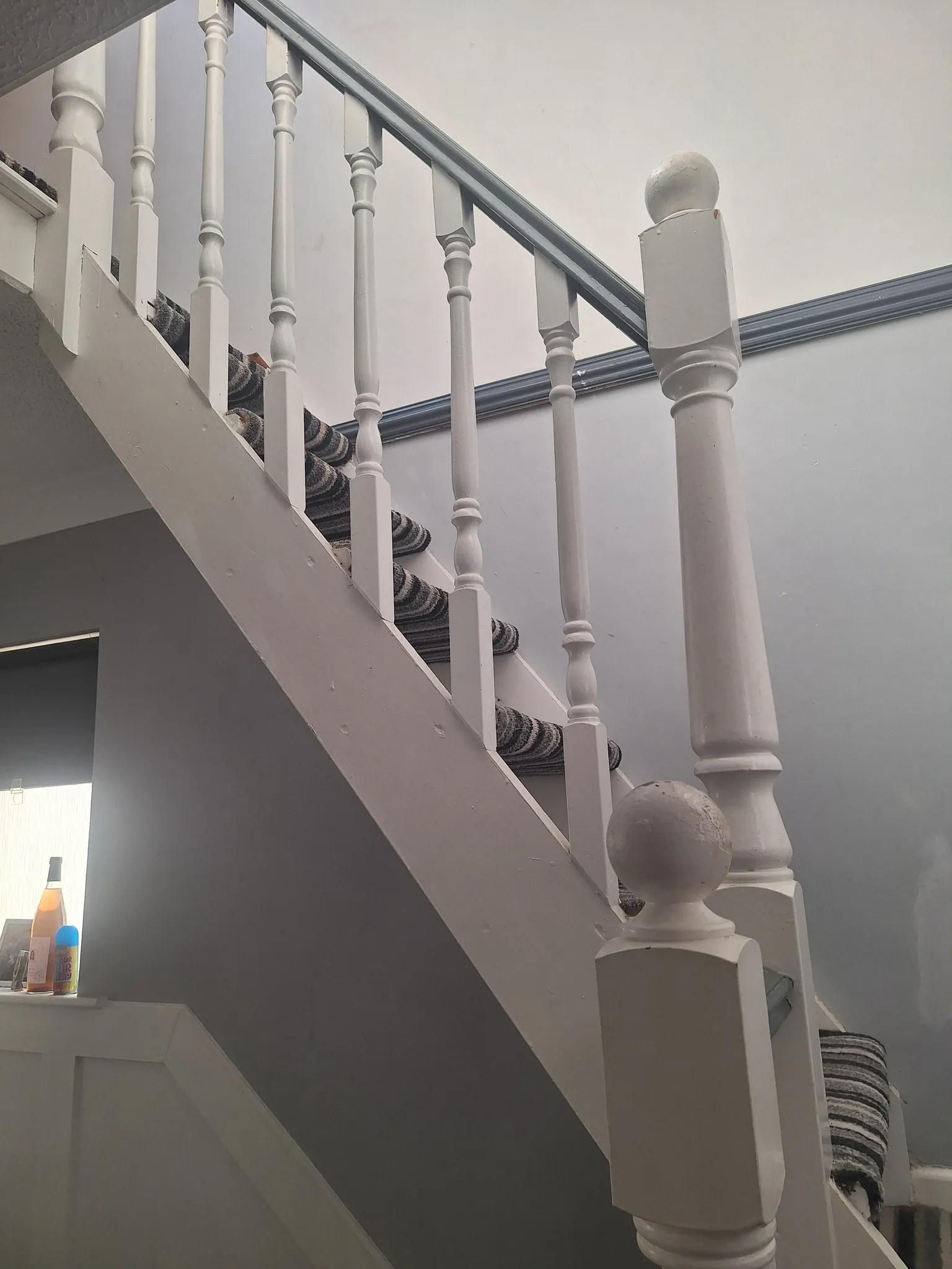 Interior stairway showing white painted wooden banister and spindles with a striped carpet runner on the stairs.