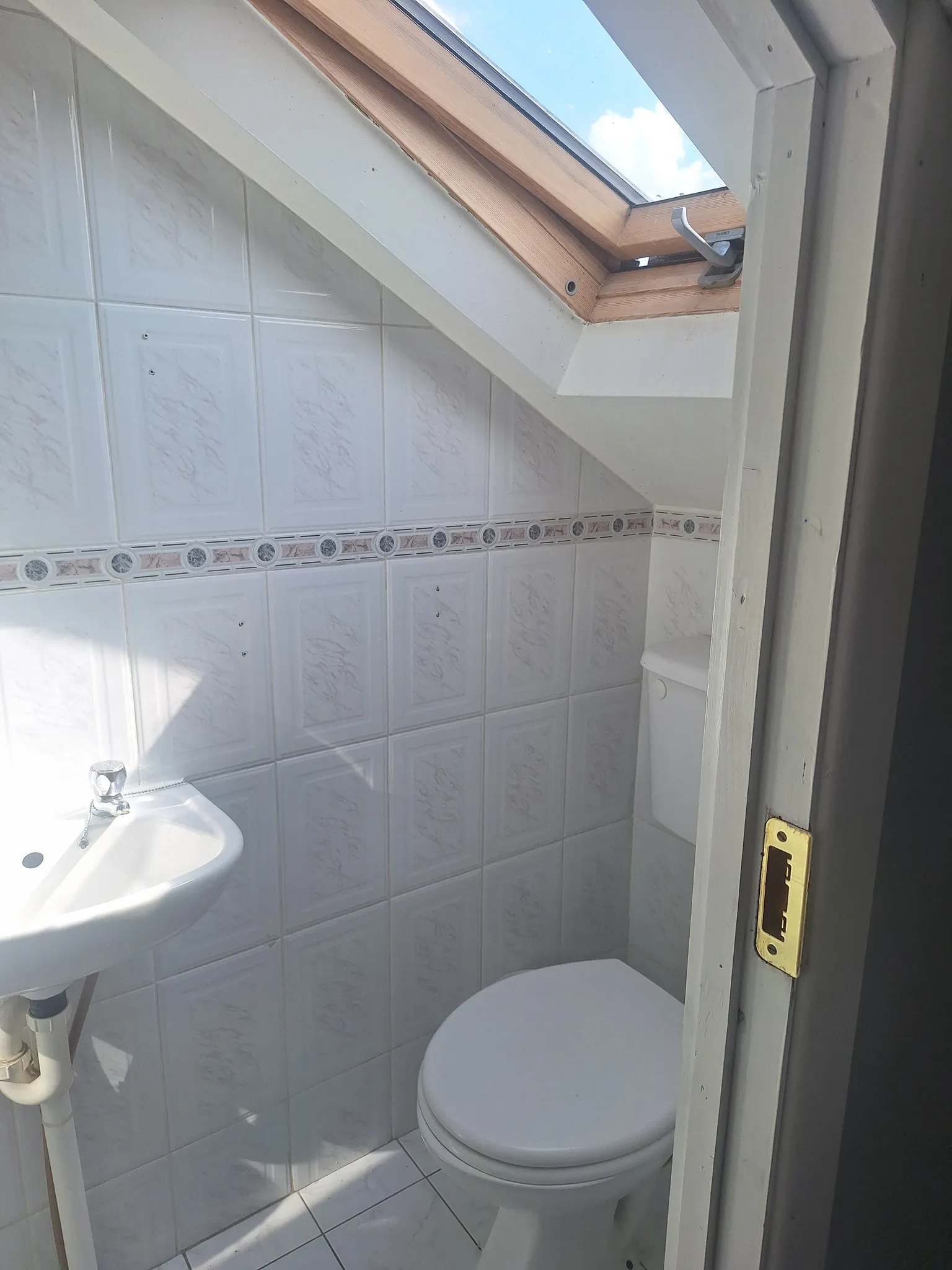 Small bathroom with a toilet, a wall-mounted sink, tiled walls and a skylight window in a sloped ceiling