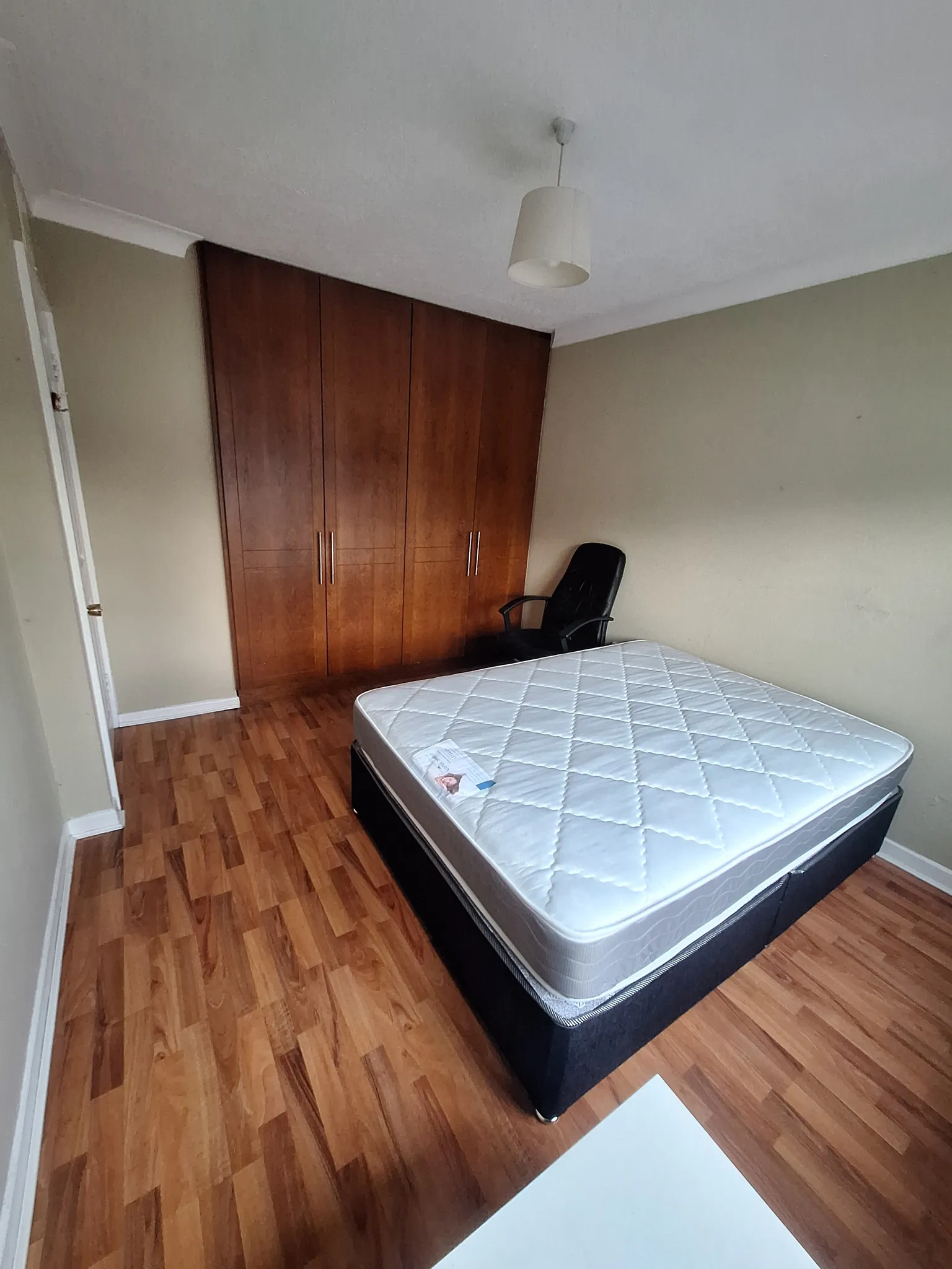 Bedroom with a mattress on a bed base, wooden built-in wardrobe, and a black office chair.