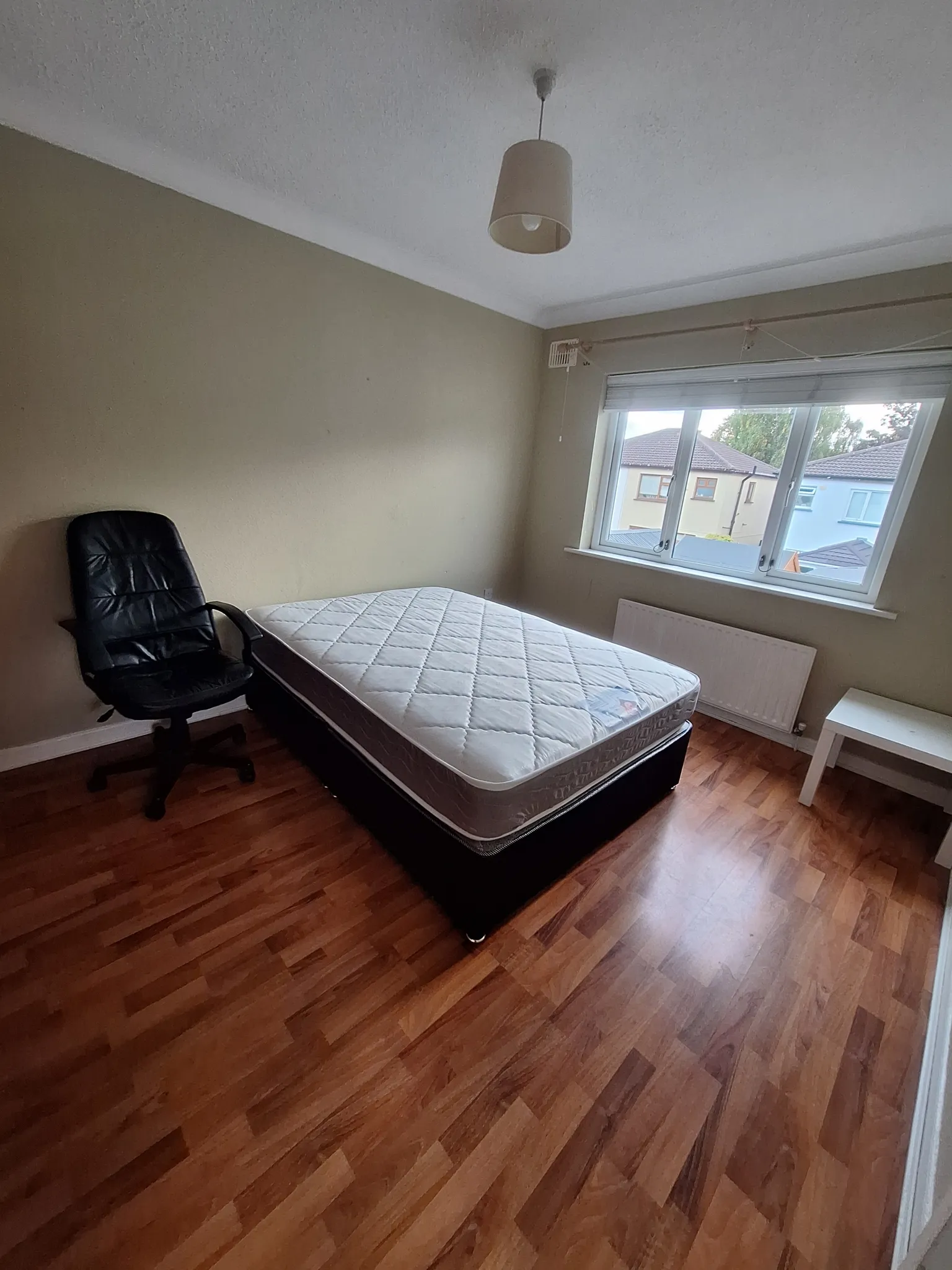 Bedroom with a mattress on a bed base, office chair, window with blinds, radiator and pendant ceiling light