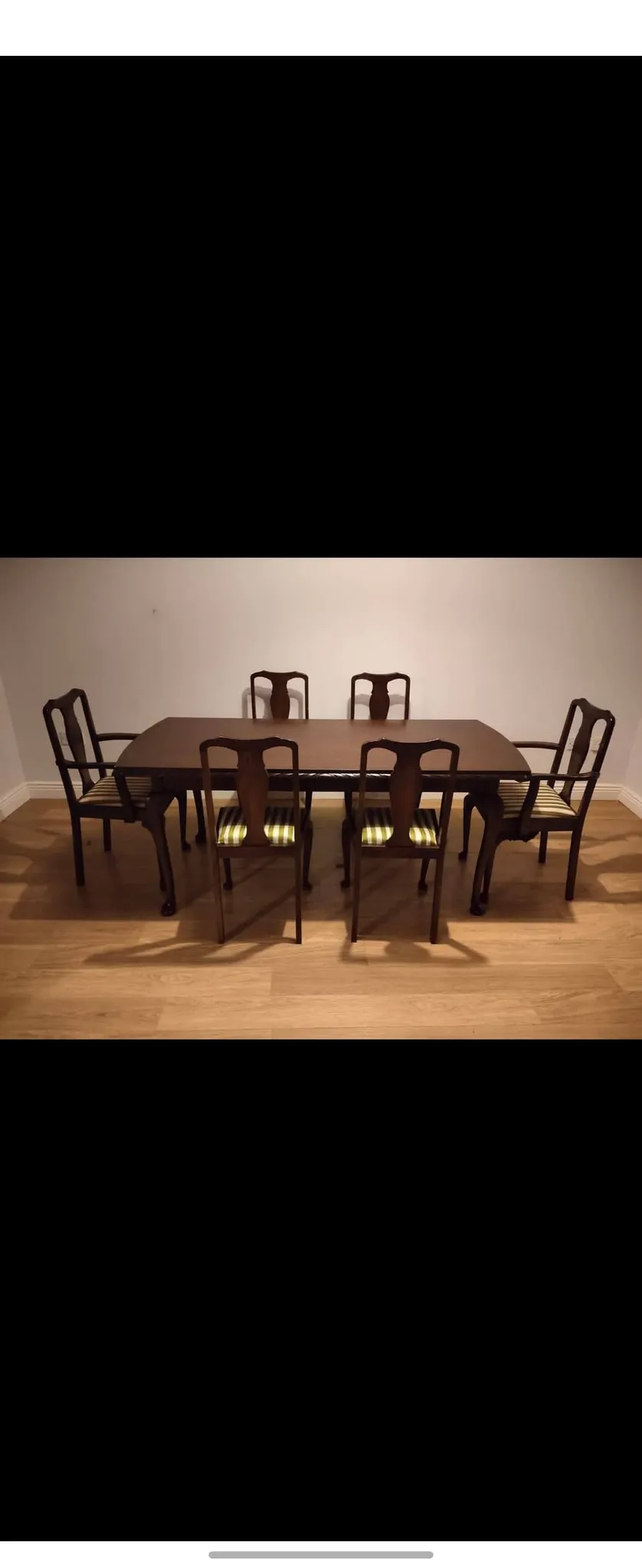Dining room with a rectangular wooden table and six wooden chairs with striped seat cushions on a hardwood floor against a plain light-colored wall.