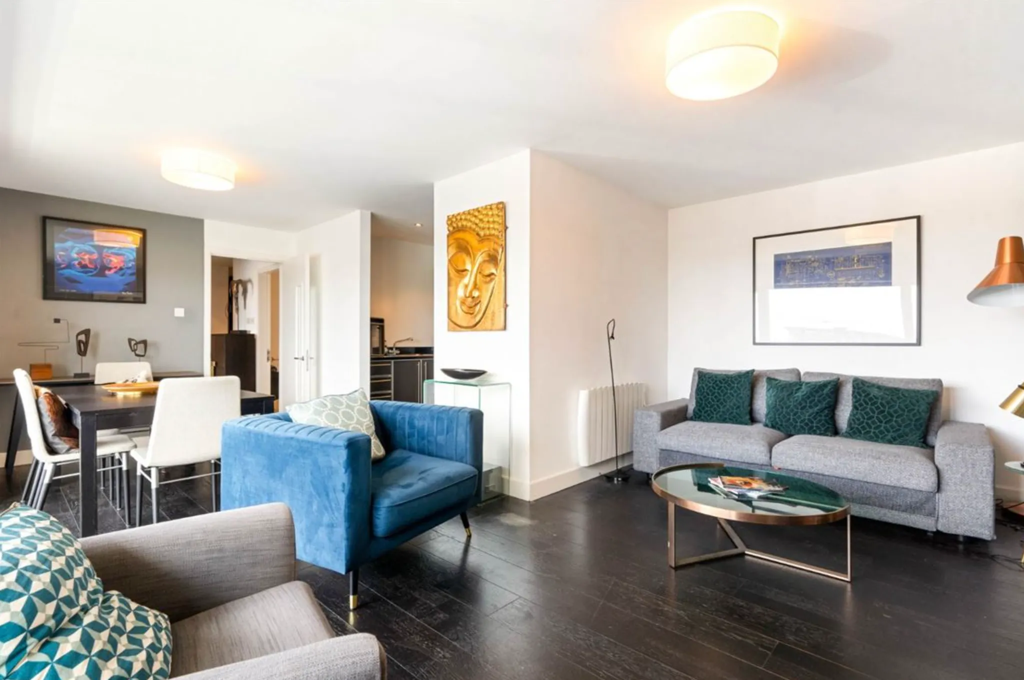 Open-plan living room with a gray sofa, blue armchair, glass coffee table, and dining table in the background