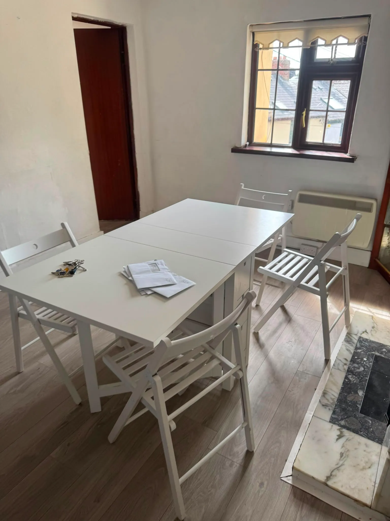 Dining room with a white folding table, four white folding chairs, a window with sill, and a doorway.