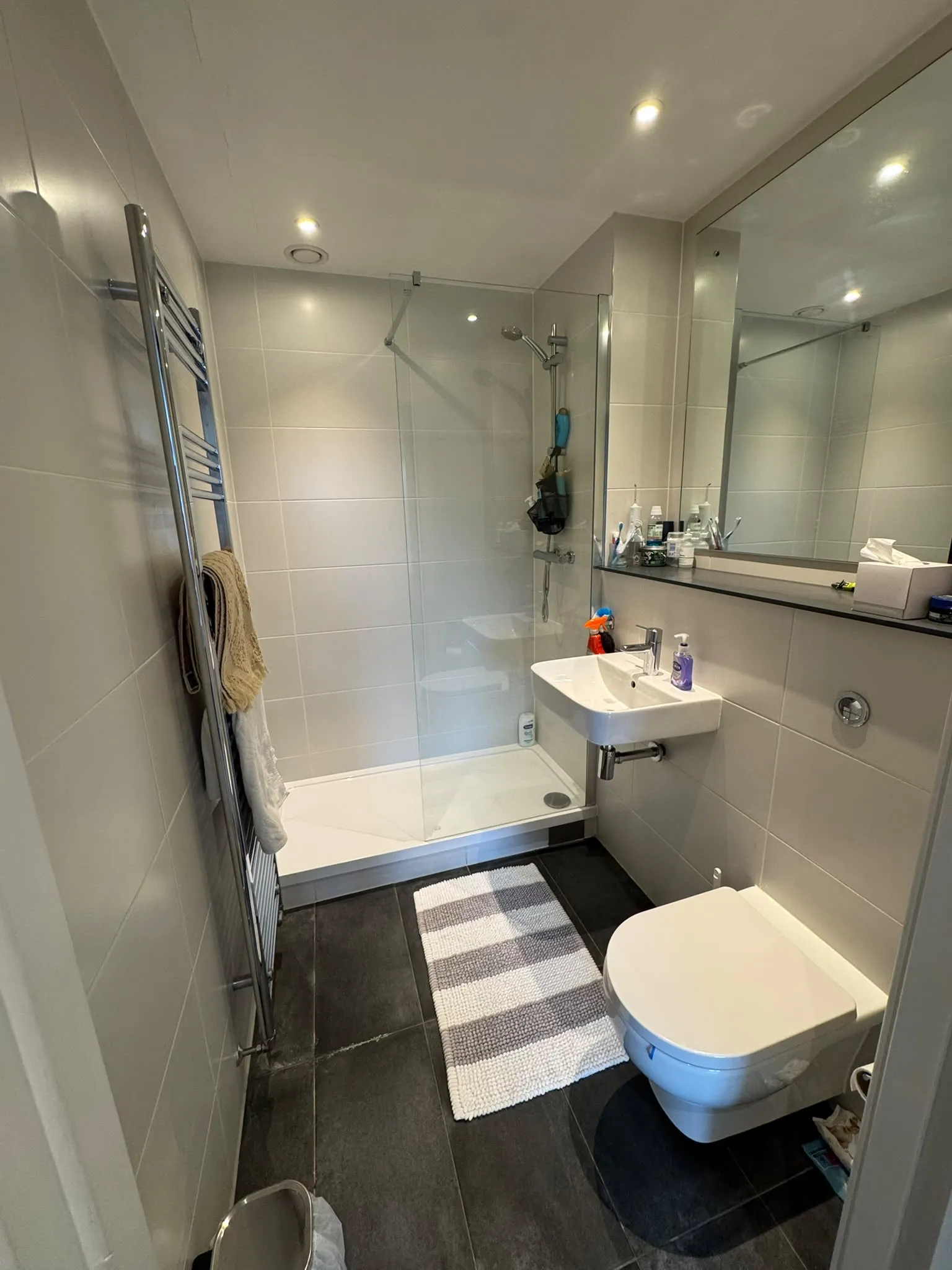 Bathroom with a walk-in shower with glass screen, wall-mounted sink and toilet, large mirror and heated towel rail.