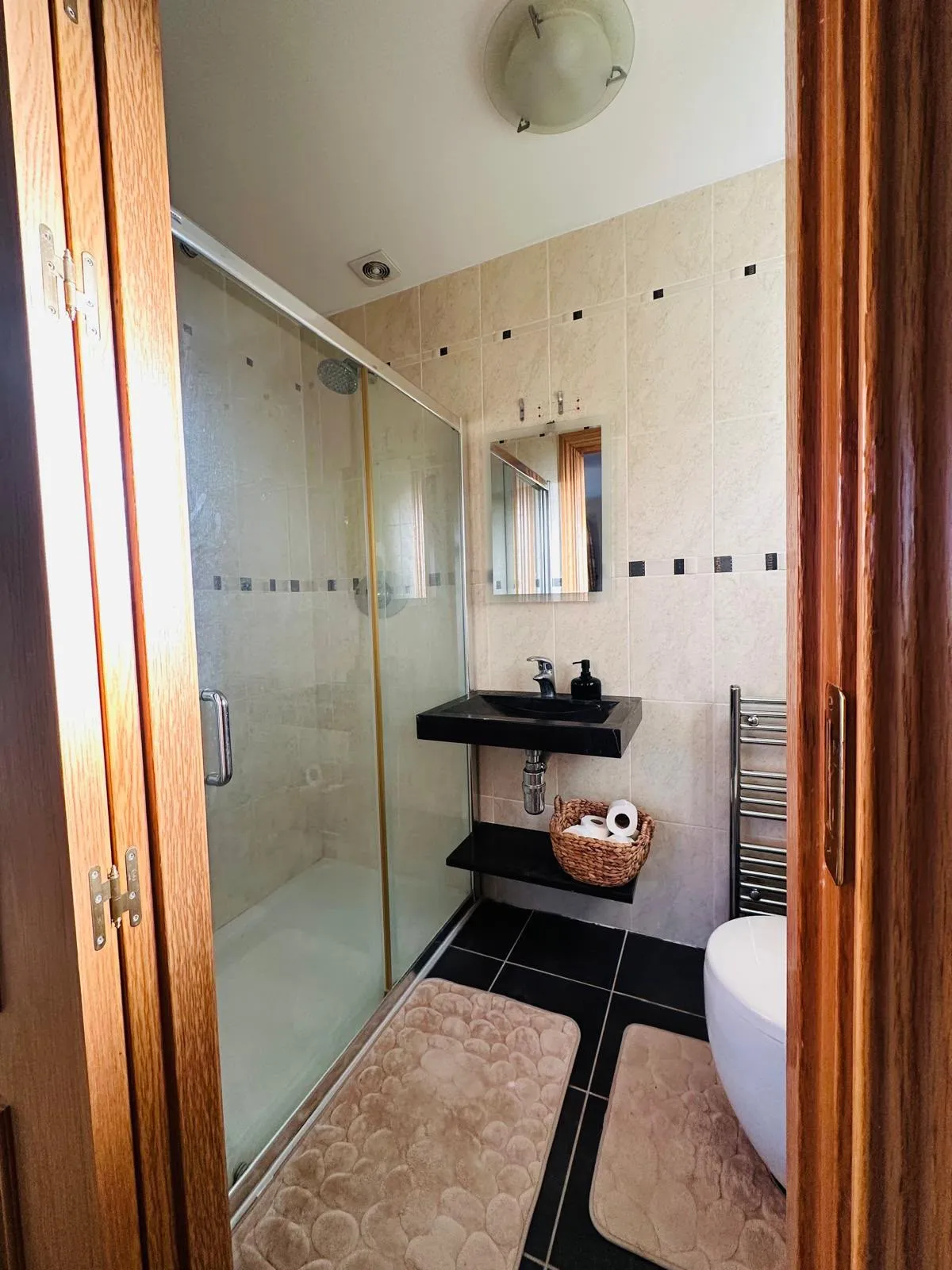 Bathroom with a glass-enclosed shower, wall-mounted black sink, mirror, towel radiator and toilet.