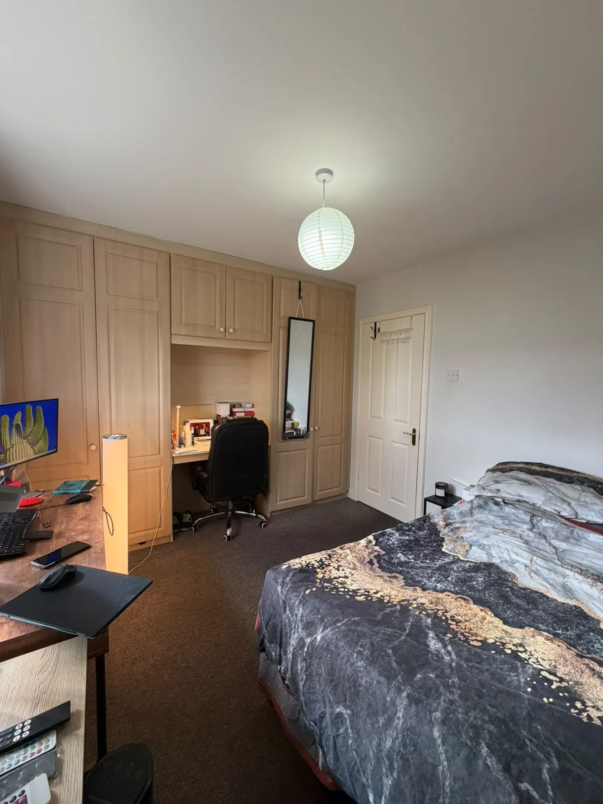 Bedroom with a double bed, built-in wardrobes with a recessed desk and office chair, a desk with a computer monitor, and a ceiling pendant light.