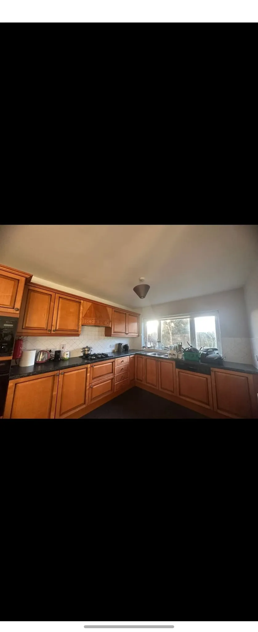 Kitchen with L‑shaped wooden cabinets, black countertop, sink under a window, and gas stove.