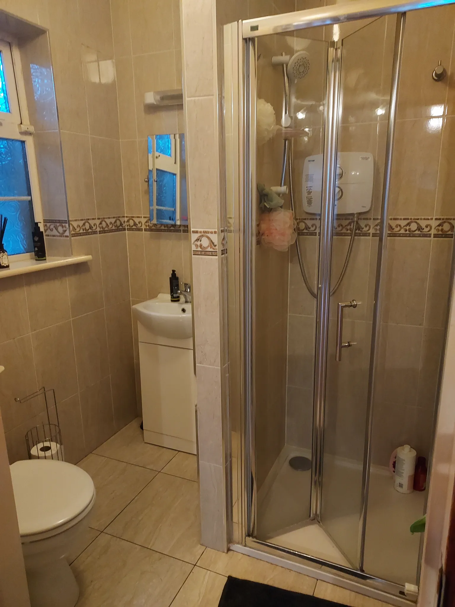 Bathroom with a corner glass shower enclosure, sink with cabinet, toilet, tiled walls and a frosted window