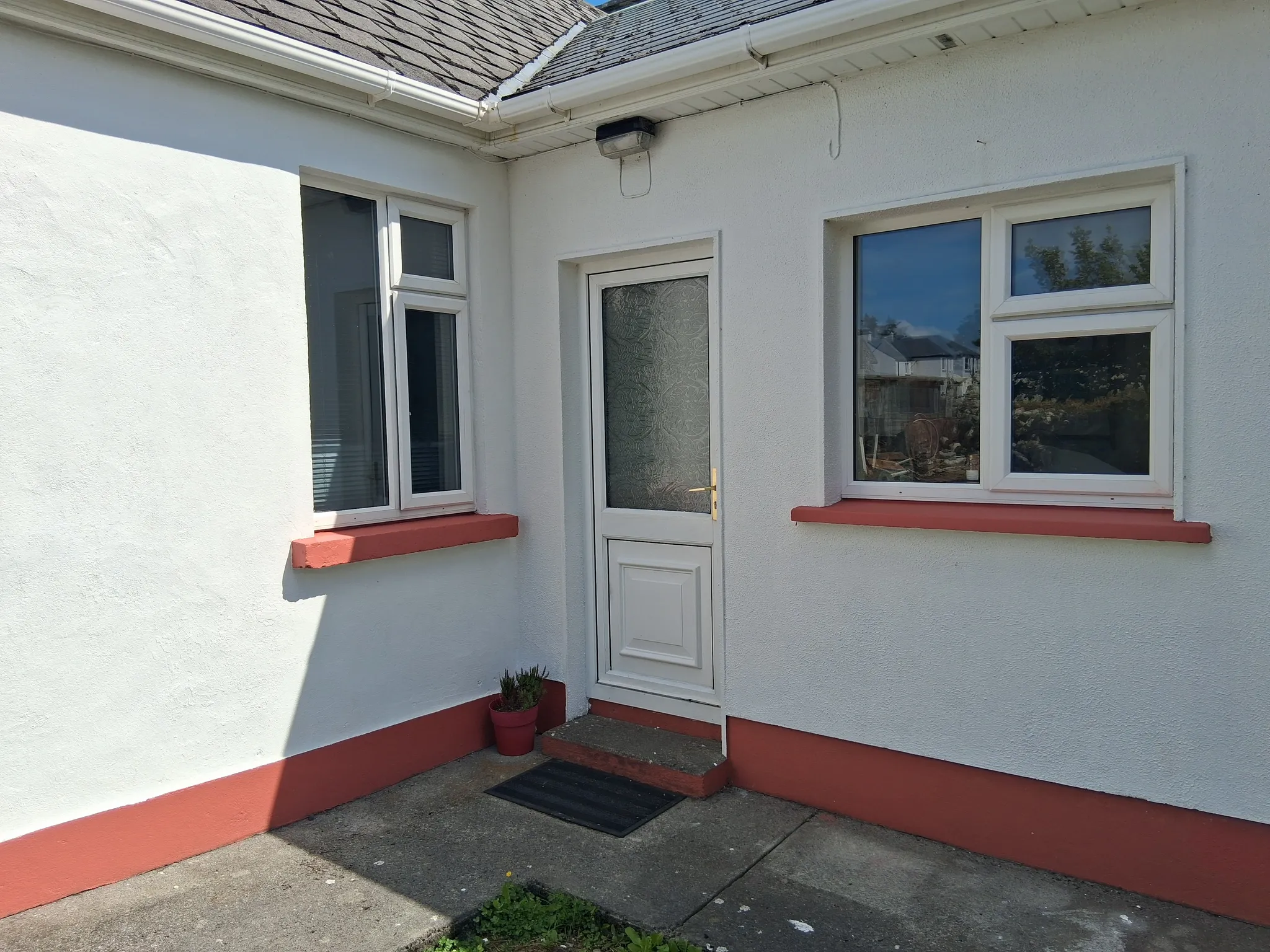 Exterior view of a white-painted entry area with a white door, two windows with red sills, a small step and a black doormat.