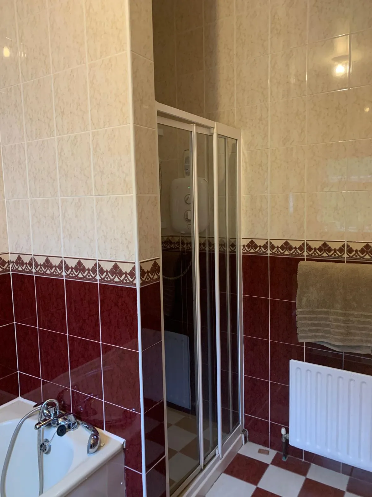 Bathroom with a corner shower with sliding glass doors, a bathtub with handheld faucet, tiled walls and a towel on a radiator.
