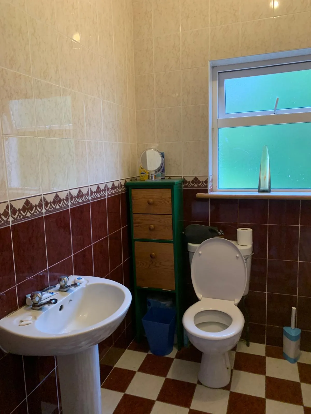 Bathroom with a toilet (seat up), pedestal sink, tiled walls and a frosted window with a vase on the sill