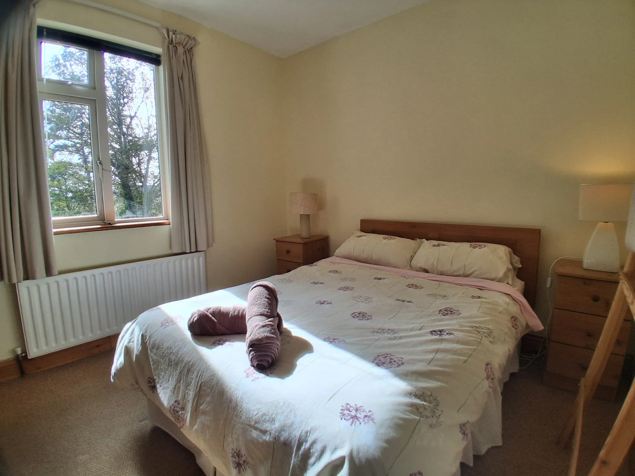 Bedroom with a double bed, two bedside tables with lamps, a window with curtains, and a radiator.