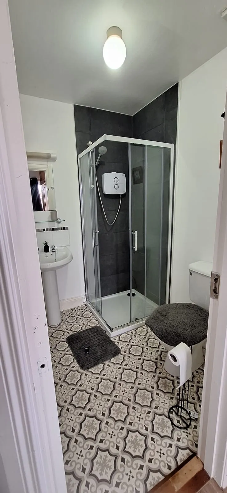 Bathroom with glass corner shower, pedestal sink with mirror, toilet, patterned tile floor, and ceiling light.