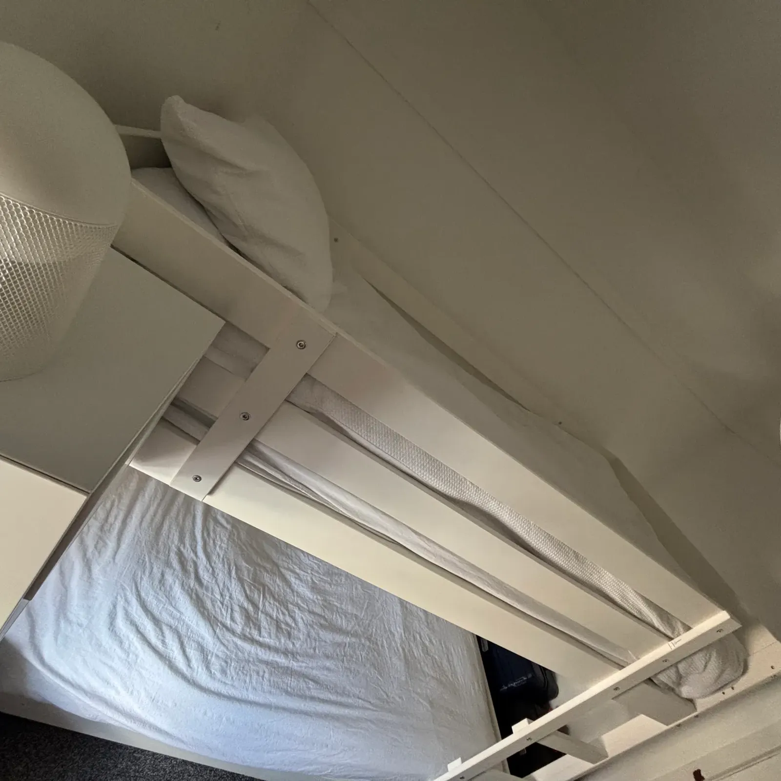 Bedroom view of a white bed with guardrail and mattress, white pillow, small bedside lamp and part of a cabinet.