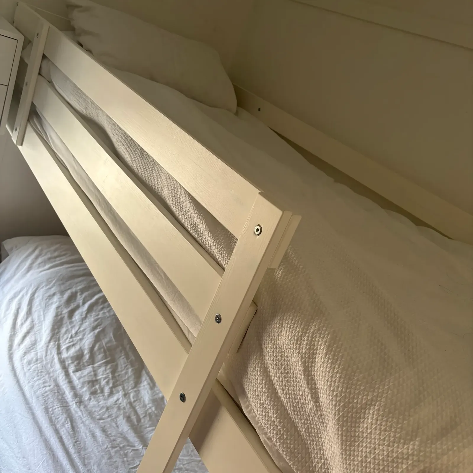 Bedroom with a light-wood bunk bed frame, white bedding and pillows, photographed at an angle