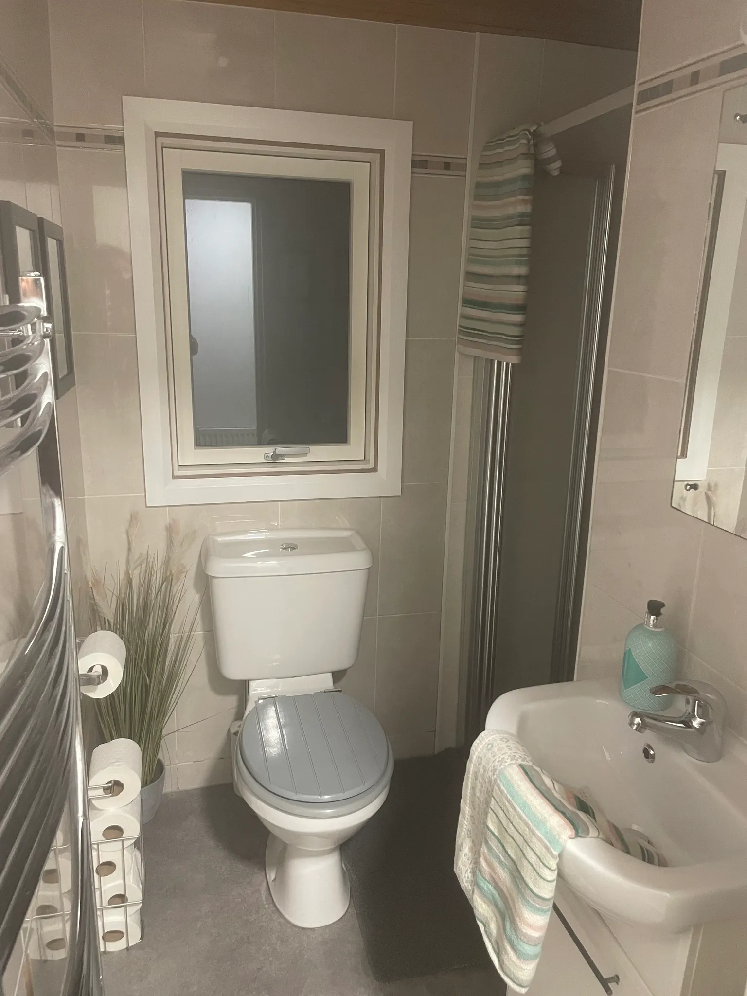 Bathroom with a toilet, small sink, window, towel on a rail and shower door